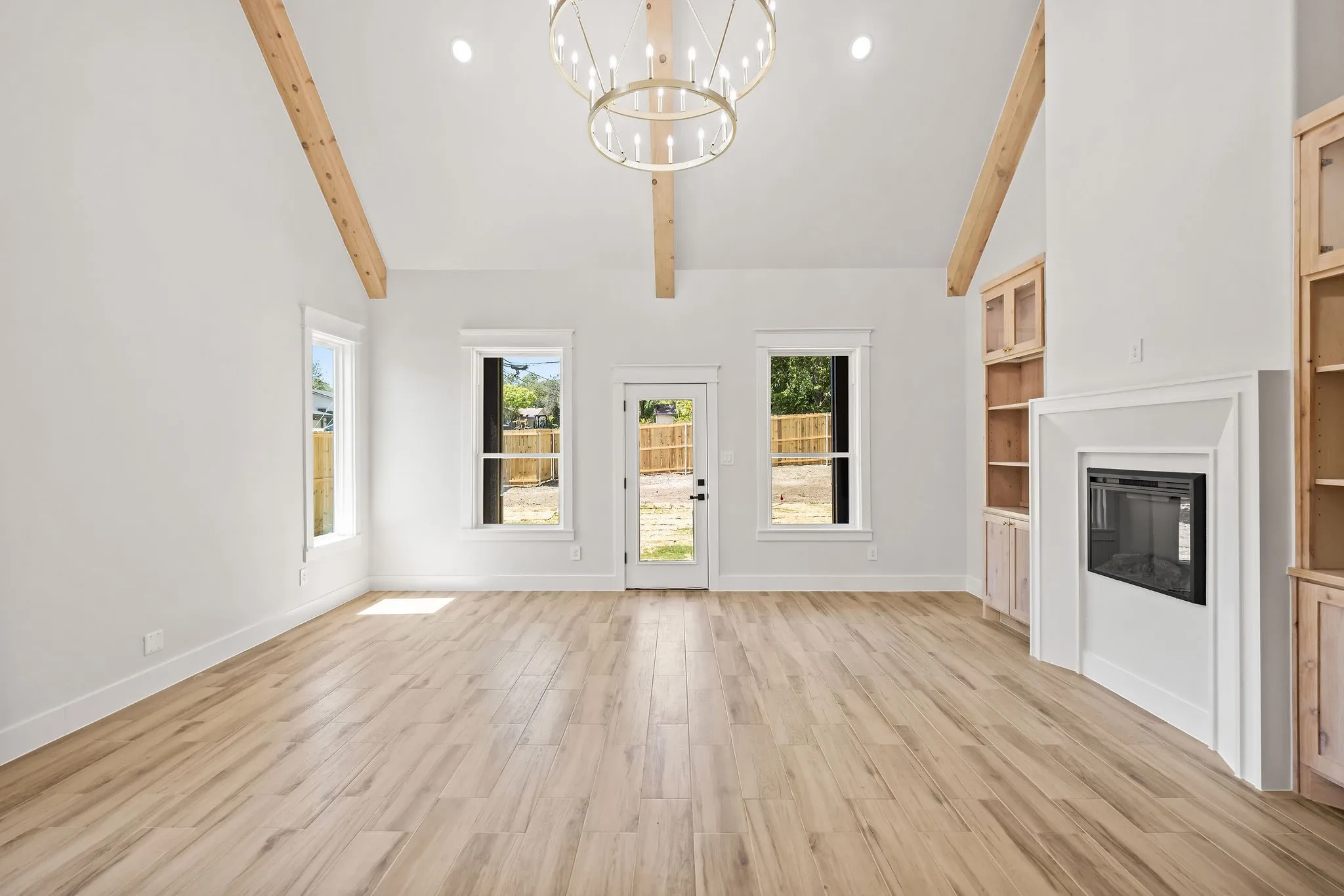 Vaulted ceilings with exposed wood beams, wood-finish flooring, fireplace, built-in cabinetry, and a contemporary chandelier