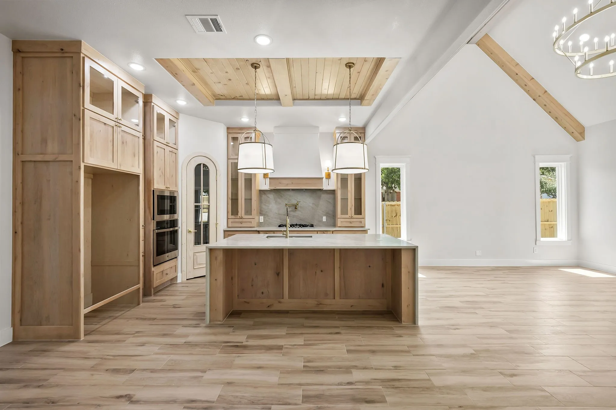 Gourmet kitchen featuring custom cabinetry, a spacious island with a sink, double wall ovens, and a wood-paneled ceiling accent
