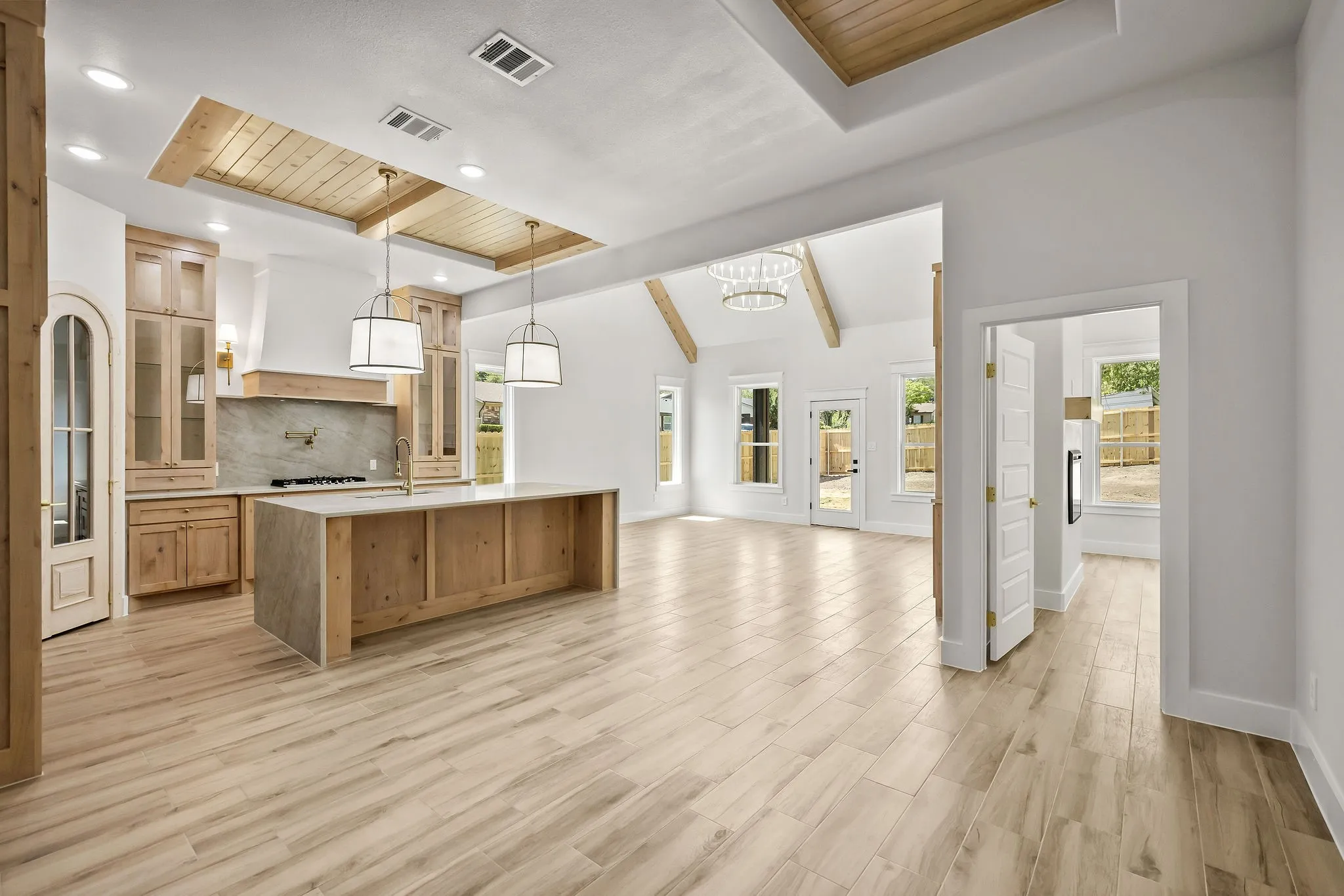 Spacious open-concept living area with wood-finish flooring, vaulted ceilings with wood beams, and a kitchen featuring a large island, wood cabinetry, and recessed lighting