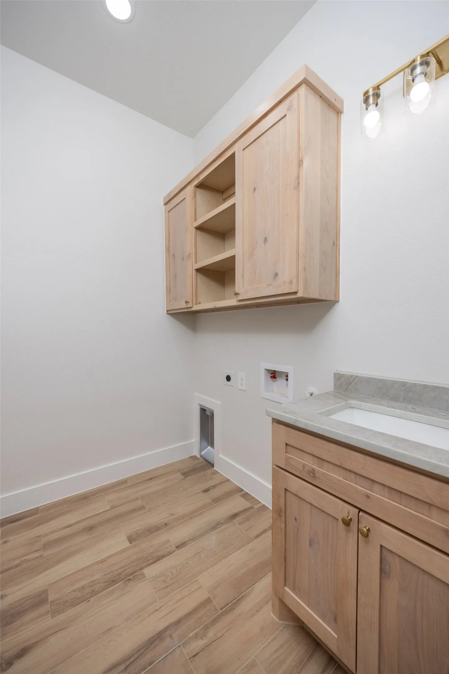 Wood-finish flooring, light wood cabinetry with open shelving, integrated sink, and granite countertop