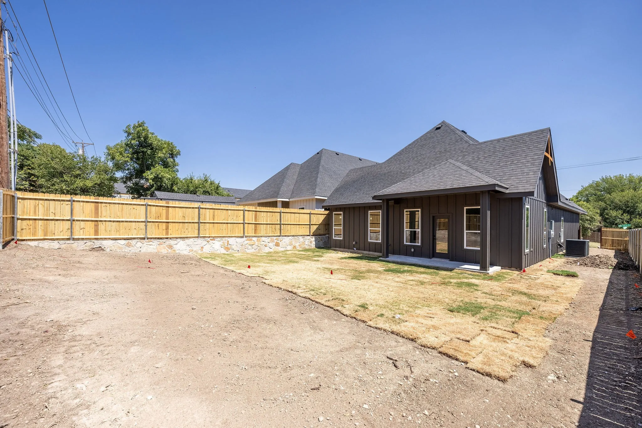 Newly constructed residence featuring a dark gray exterior, white window trim, a covered patio, and a shingled roof