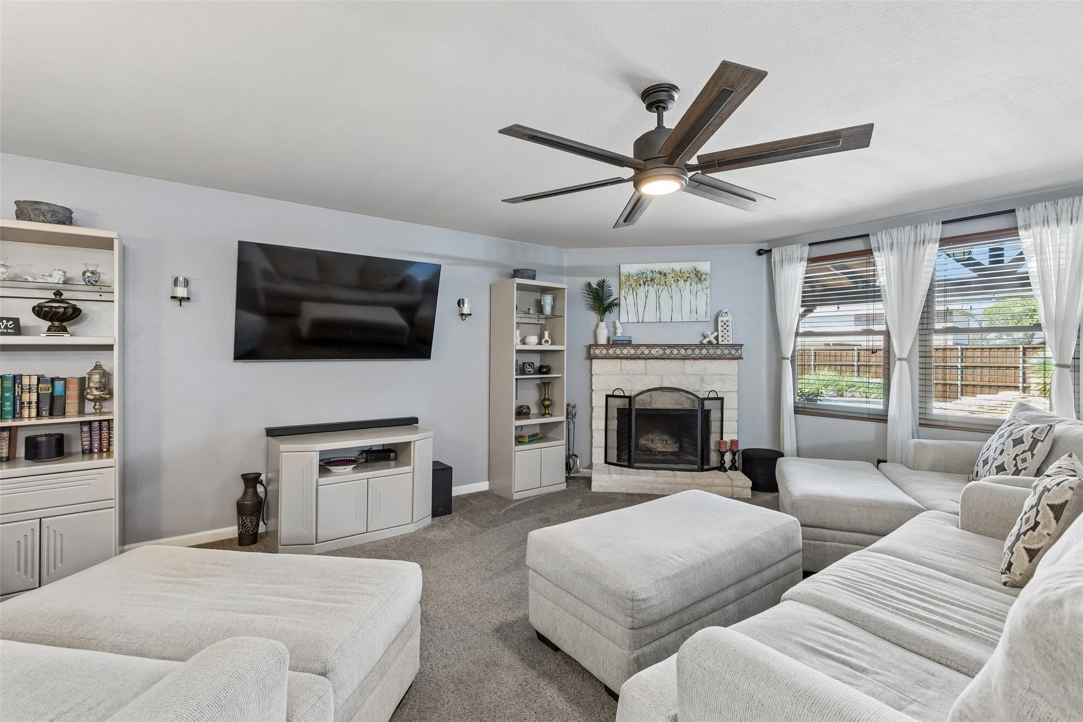 A Family Room Built for Everyday Living – The spacious family room is anchored by an Austin stone fireplace, with two large windows overlooking the covered patio and bringing backyard views into the heart of the home.