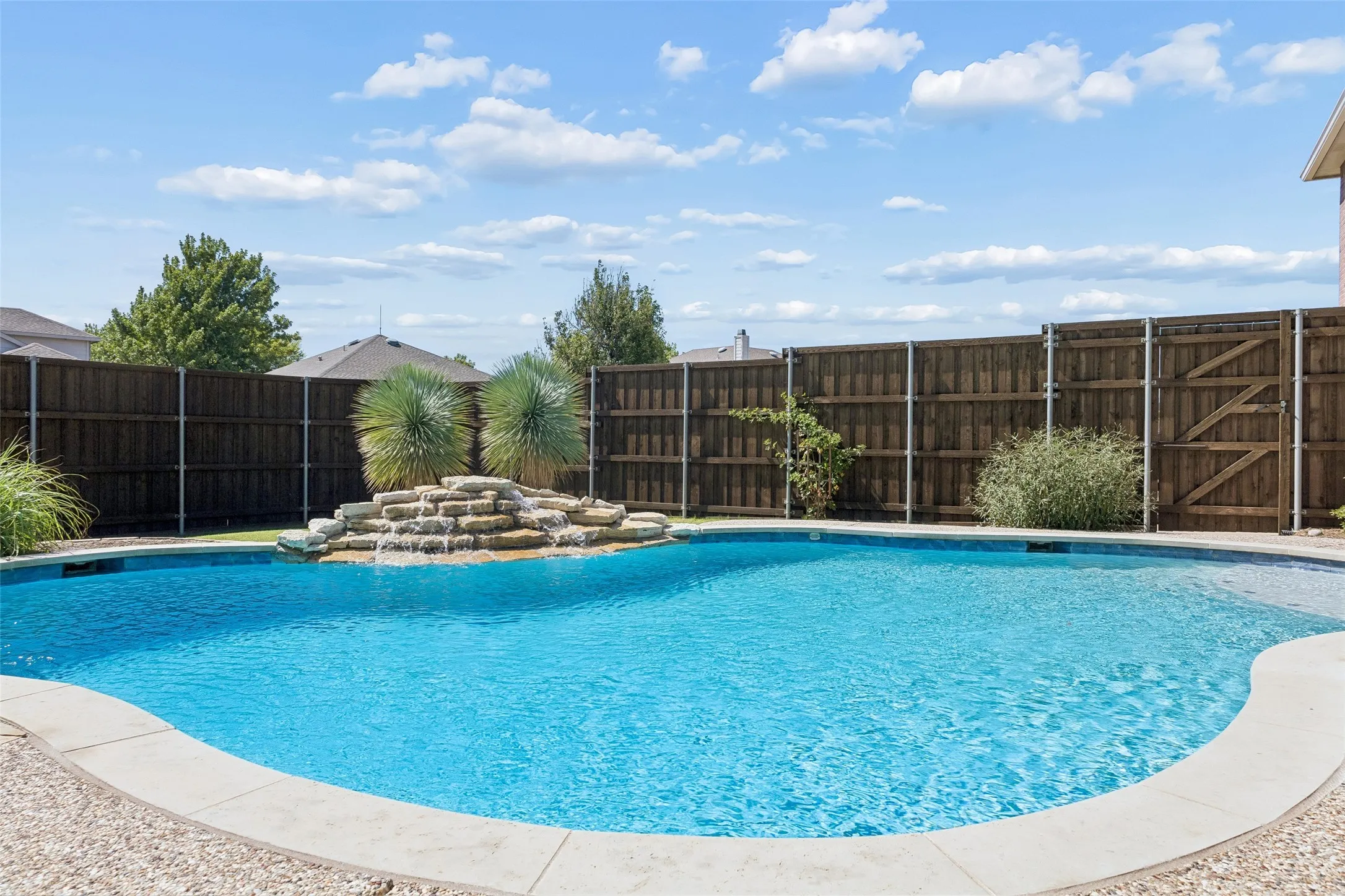 Your Own Backyard Escape – The pool’s curved design, cool-deck surround, rock waterfall, and surrounding lawn come together to create an outdoor space made for warm Texas afternoons and relaxed evenings at home.