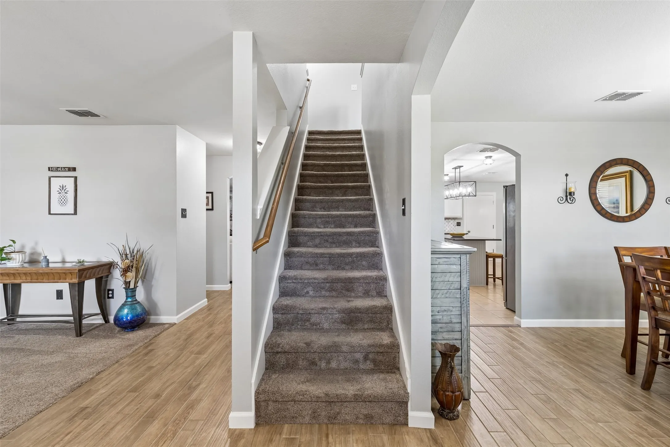 A Layout That Connects the Home – The central staircase separates the formal living and dining spaces while arched openings and wood-look tile create an easy transition between the entry, kitchen, and main living areas.
