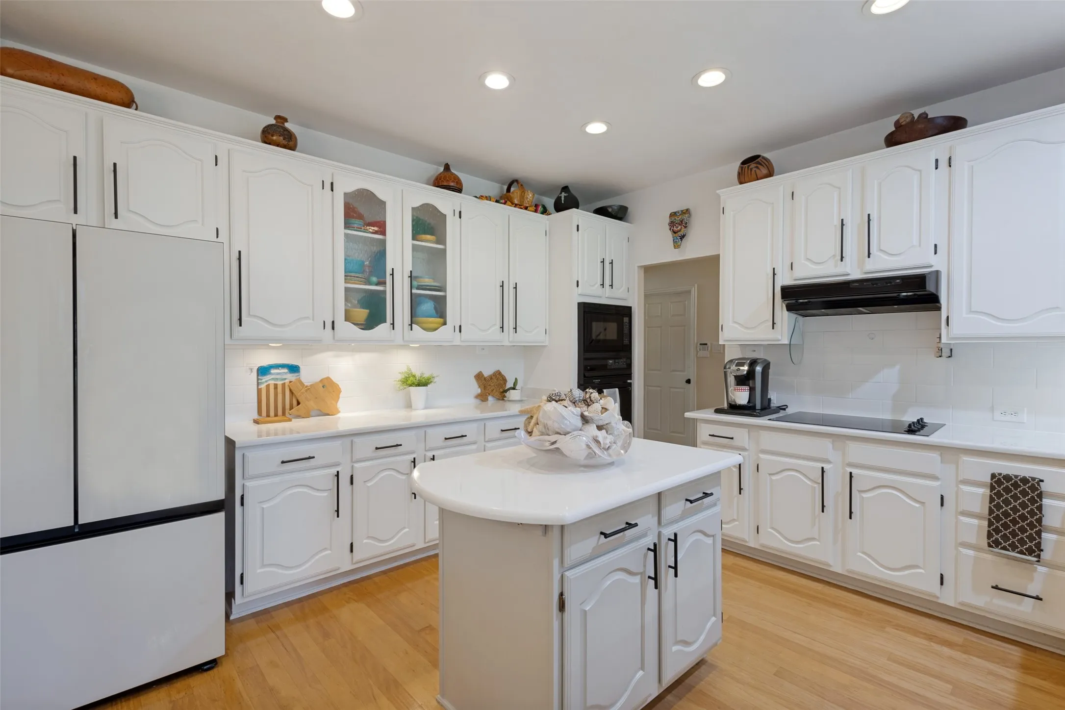 Quartz counter tops, white subway tile bkspl. Includes the recent modern white Bespoke Samsung Refrigerator & Dishwasher. Fresh white cabinetry, glass displays and black iron hardware.