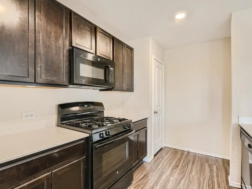 Dark wood-finish cabinetry, light countertops, built-in black microwave, and black gas range