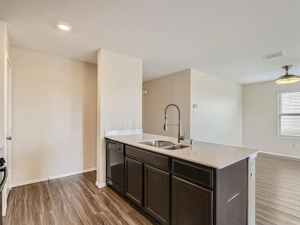 Kitchen island with dark wood-finish cabinetry, a stainless steel double sink, and a high-arch faucet