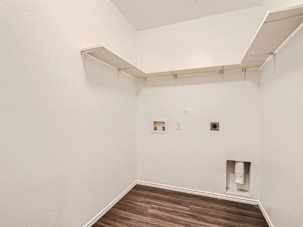 Wood-finish flooring with white baseboards, wall-mounted shelving, and utility hookups