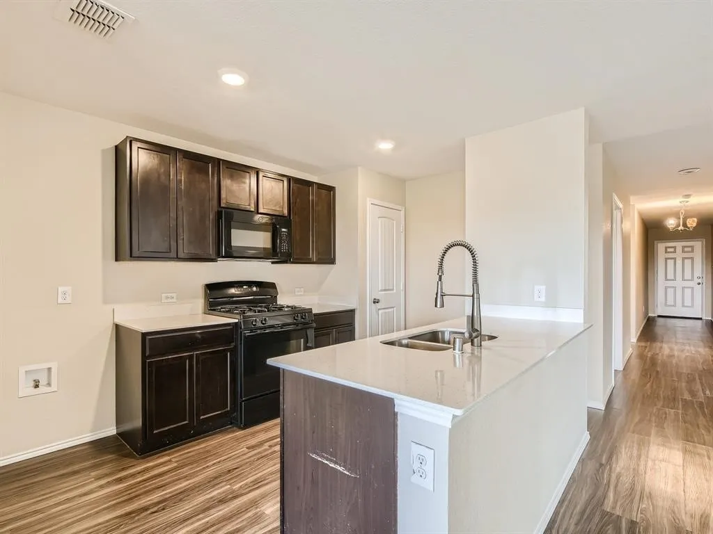 Kitchen featuring dark wood cabinetry, light countertops, stainless steel sink with gooseneck faucet, black oven range, and wood-finish flooring