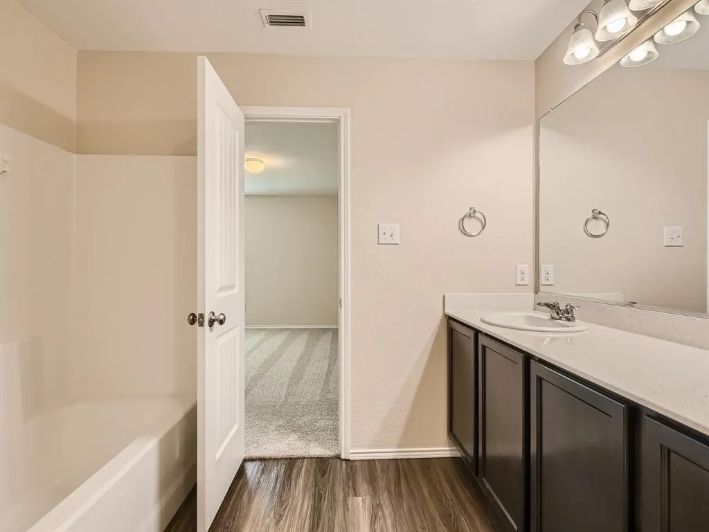 Bathroom featuring a single vanity with dark cabinetry, integrated sink, and light-toned countertop