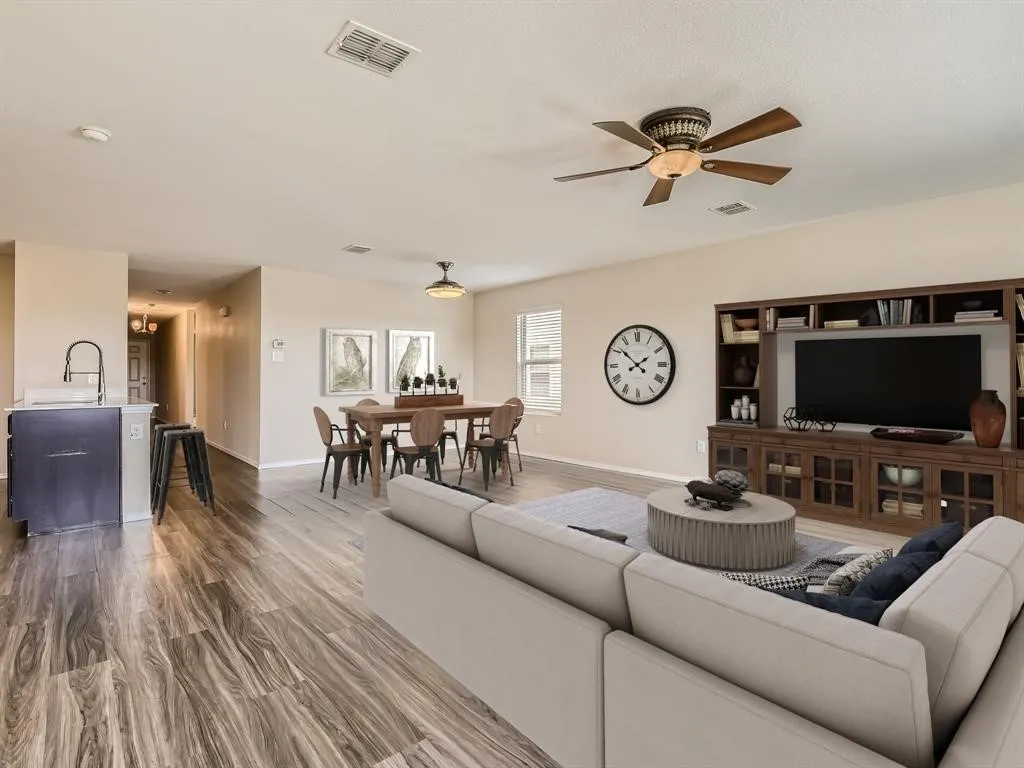 Wood-finish flooring throughout, a dining area with ceiling-mounted light fixture, a living area with a built-in media console, and a kitchen island with a single-basin sink