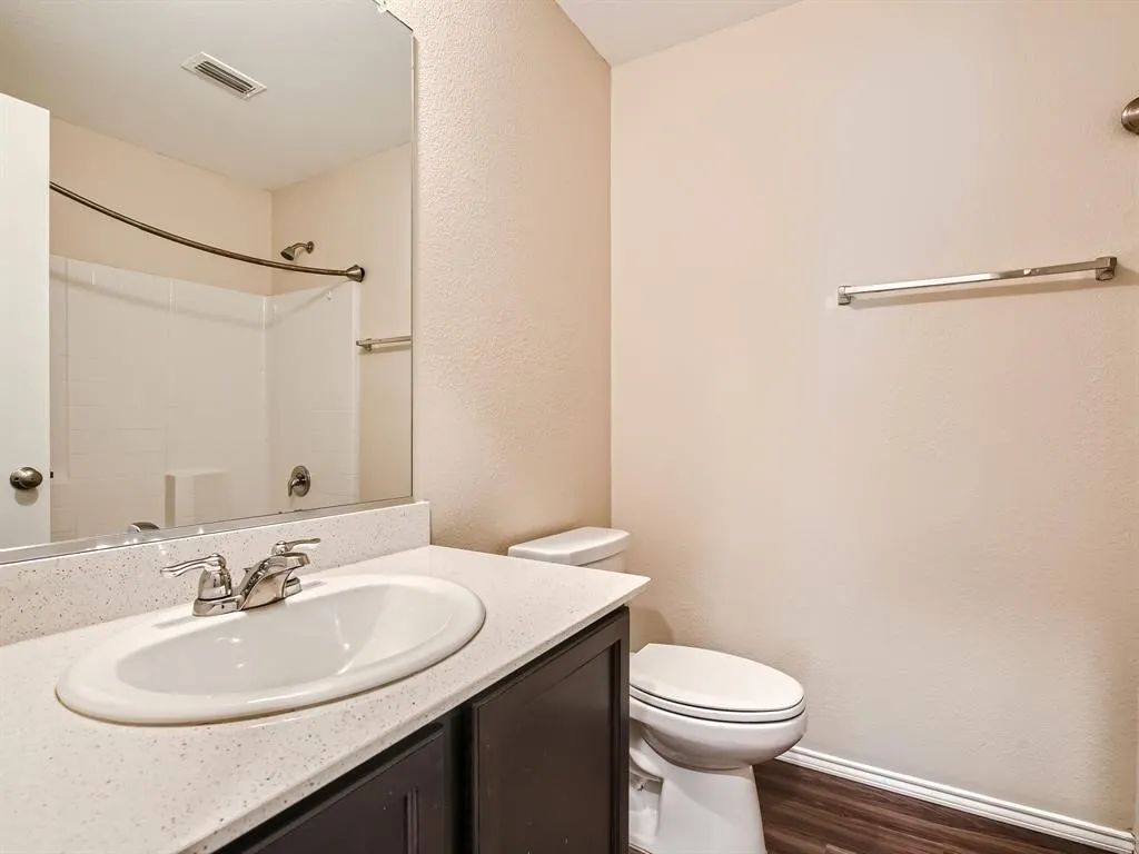 Bathroom featuring a vanity with an integrated sink, a speckled countertop, dark wood-finish cabinetry, and wood-finish flooring