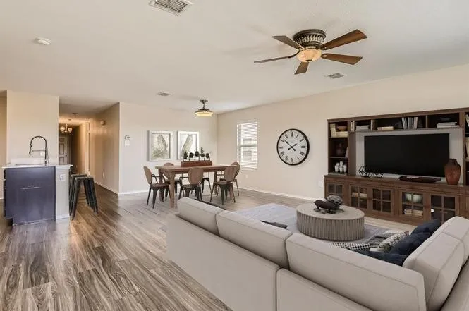 Wood-finish flooring throughout, integrated kitchen island with sink, dedicated dining area, built-in entertainment center, and ceiling fan with lighting