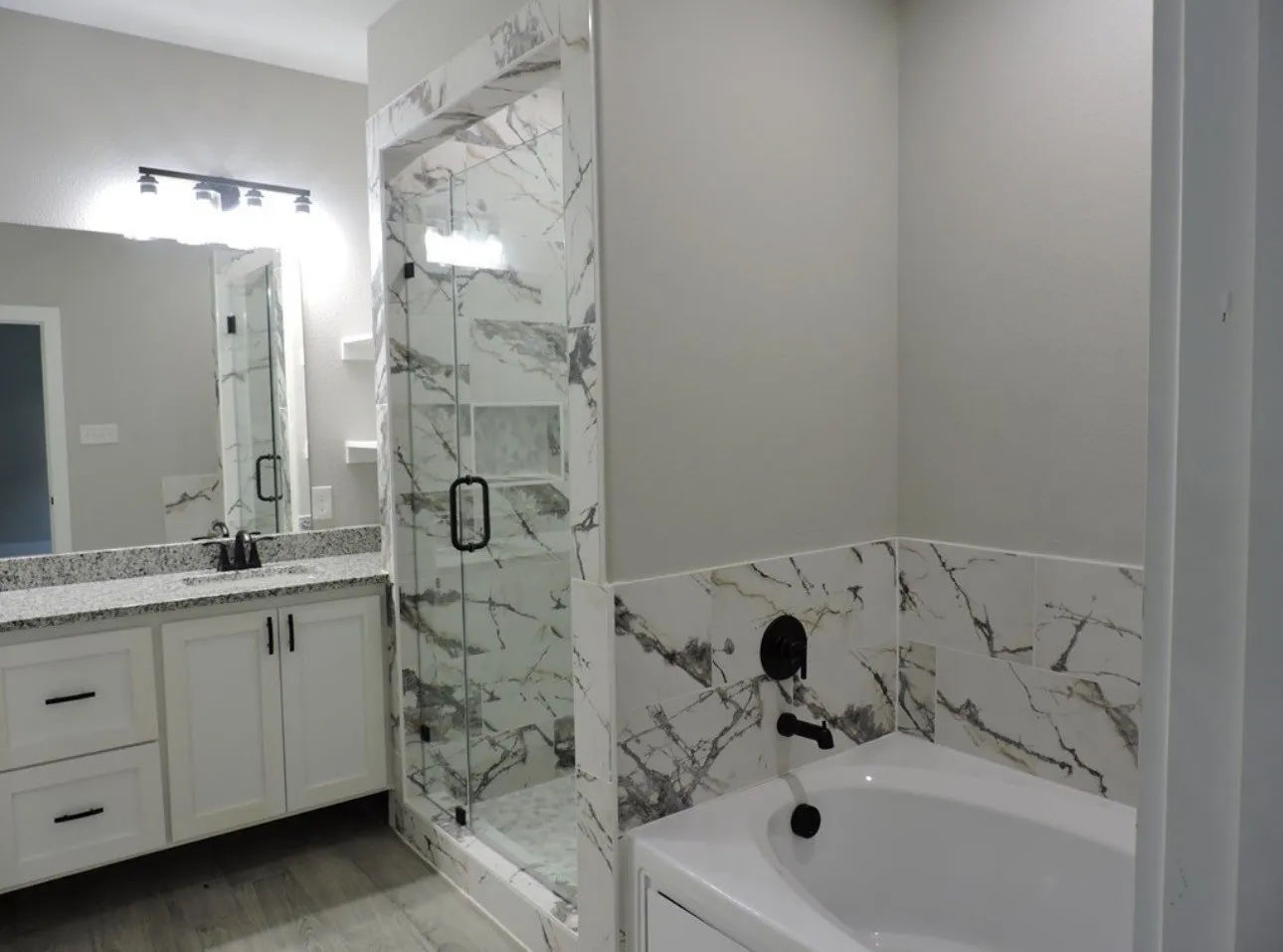 White vanity with granite countertop, wood-finish flooring, and a walk-in shower with glass enclosure