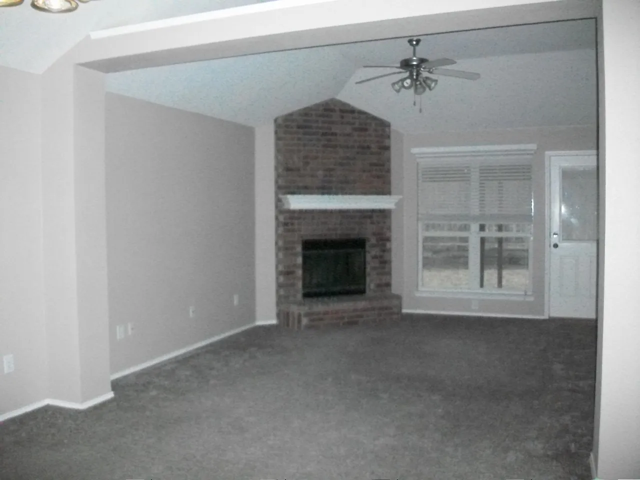 Vaulted ceiling, brick fireplace with mantel, ceiling fan, double window with blinds, and white paneled door