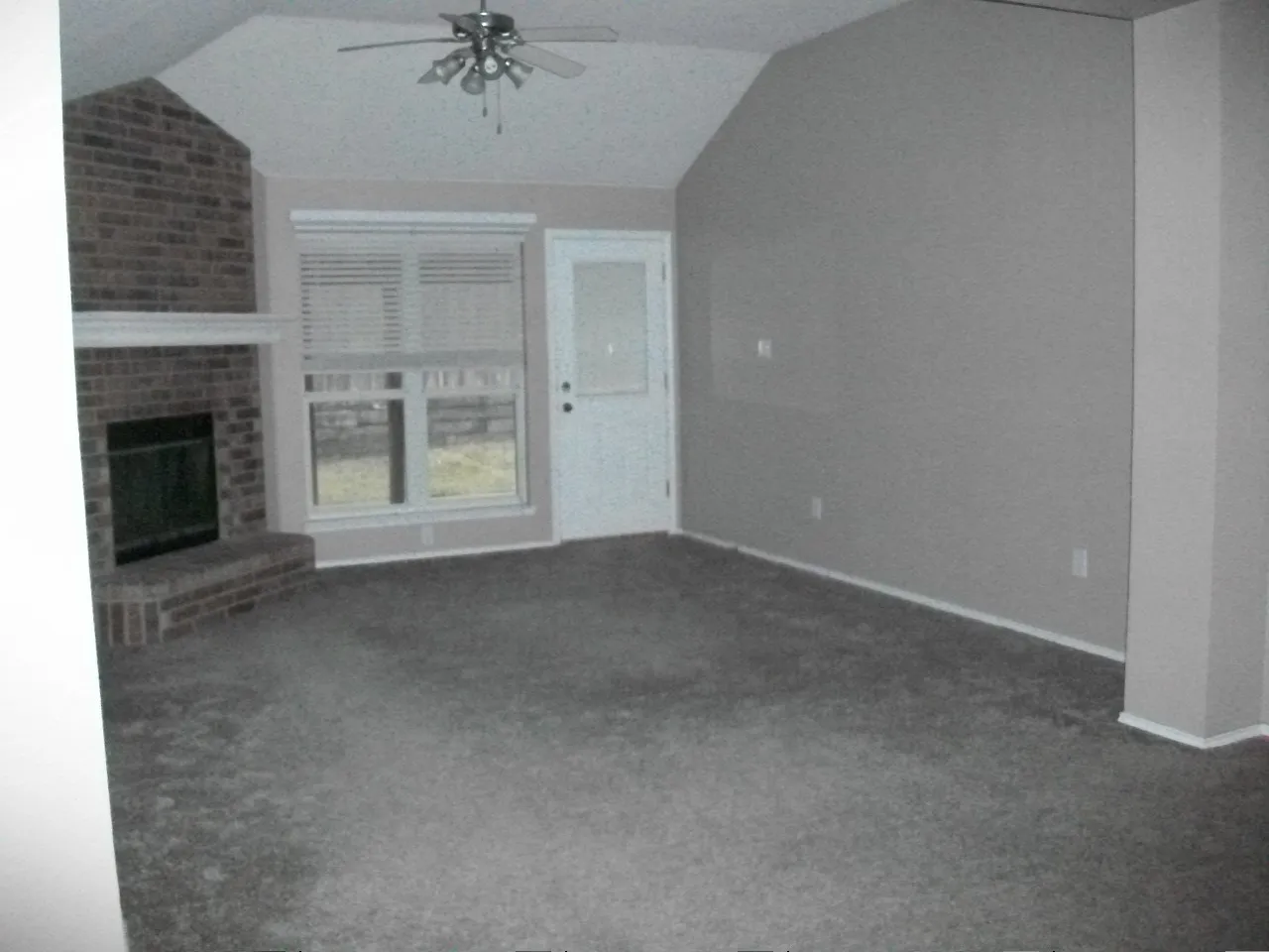 Vaulted ceiling with a ceiling fan, brick fireplace with a white mantel, and a window with blinds