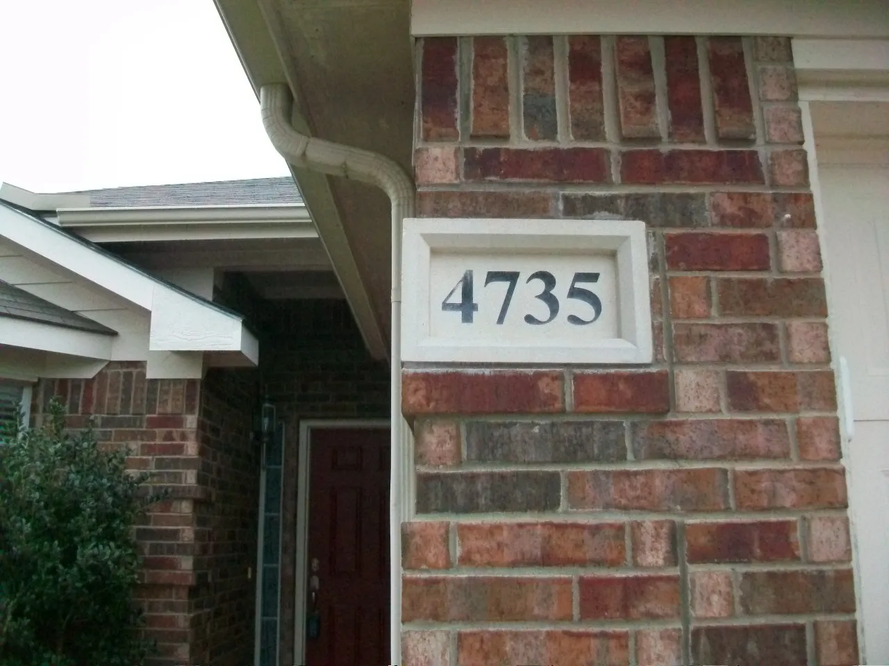 Brick exterior with a decorative address plaque, a red entry door, and a light-colored gutter system