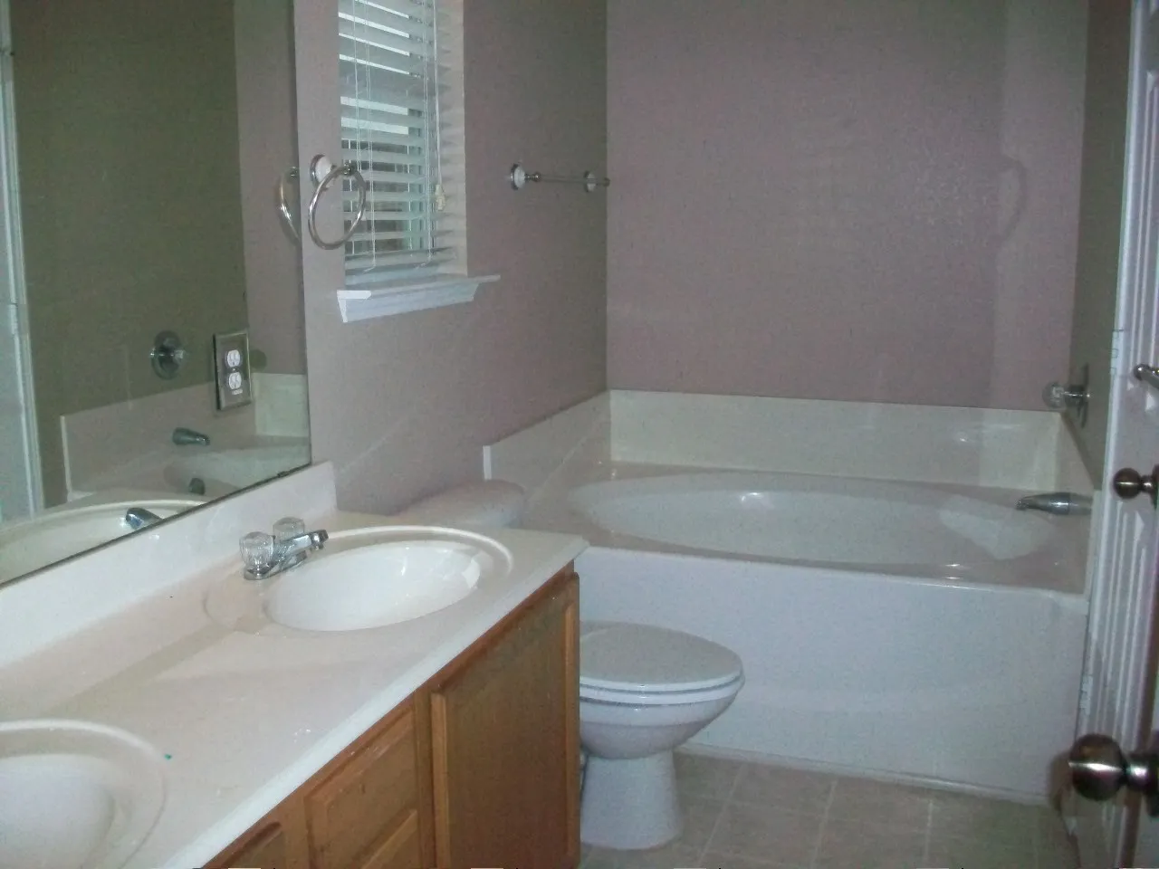 Dual vanity with integrated sinks, wood-finish cabinetry, built-in soaking tub, and tiled flooring
