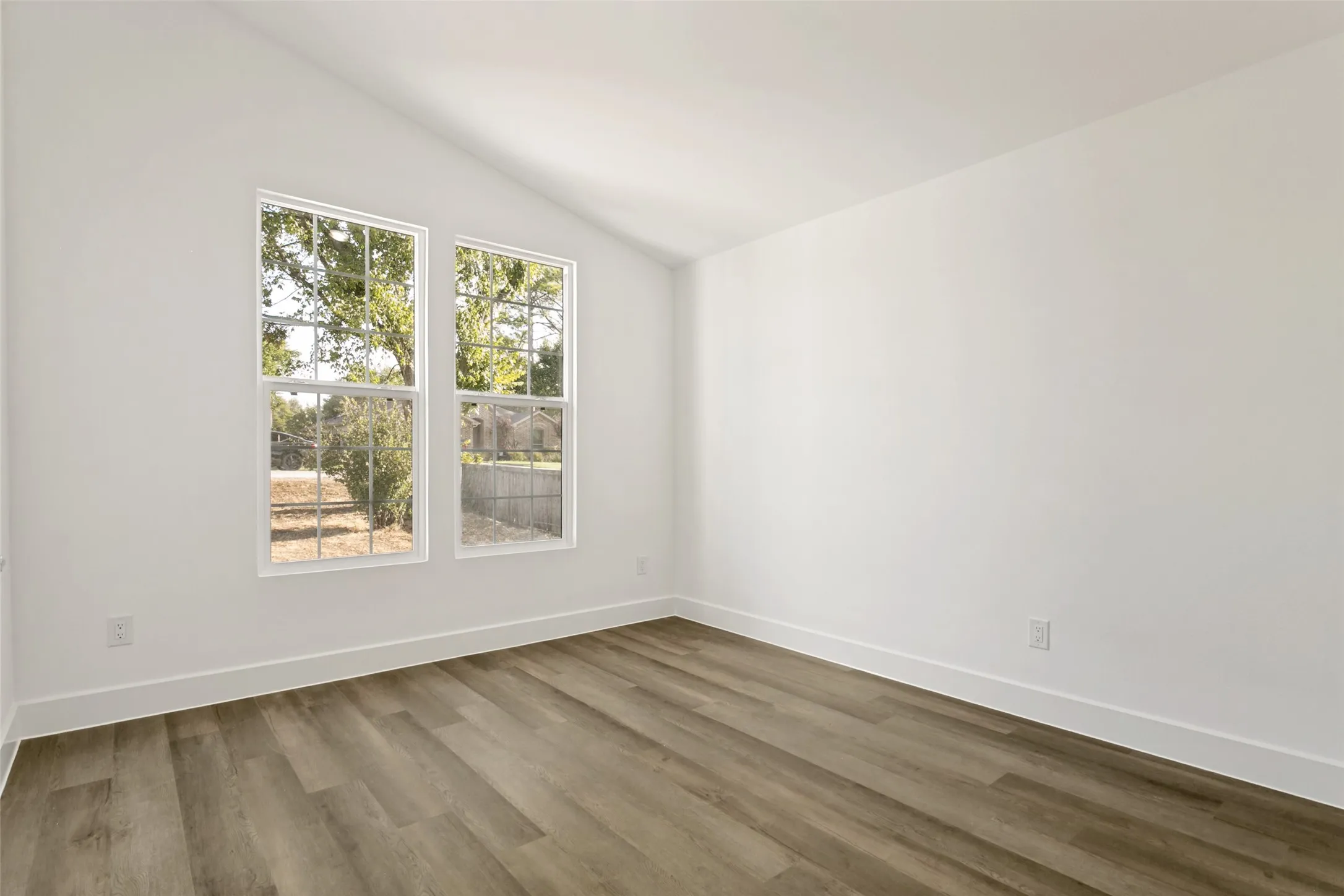 Vaulted ceiling with bright white walls, two double-hung windows, and wood-finish flooring