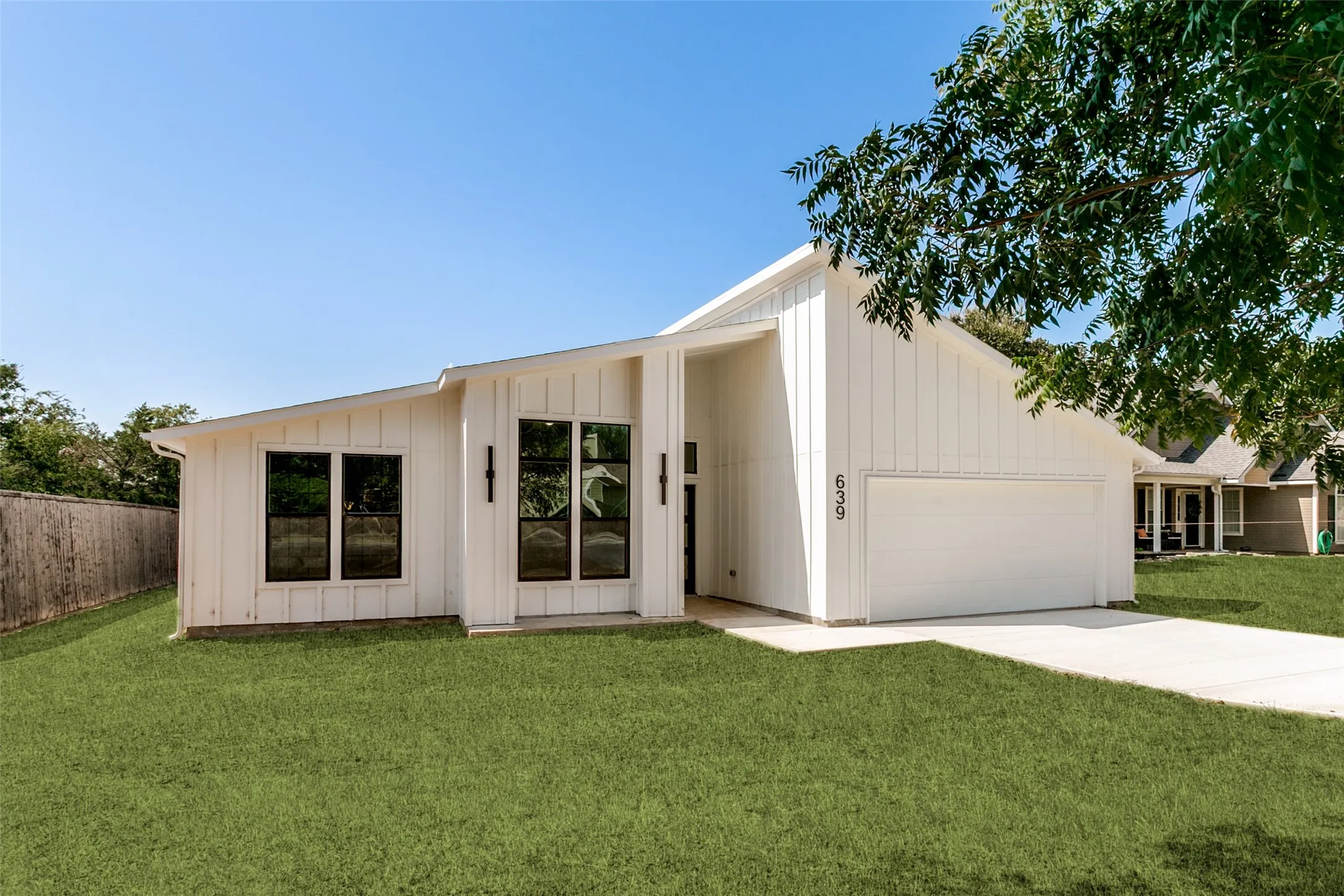Modern white board and batten exterior with black-framed windows, a covered entry, and an integrated garage