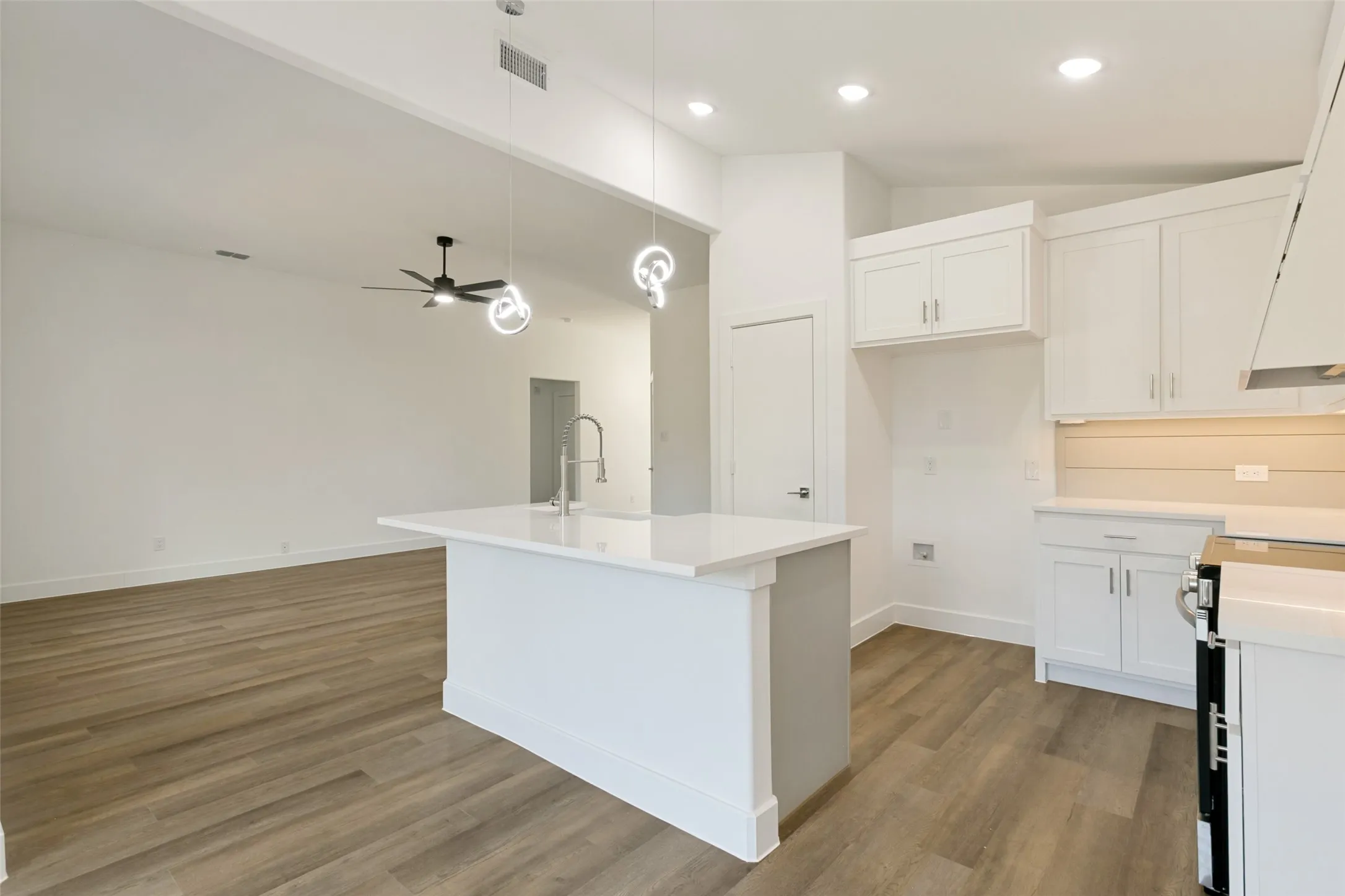 Open-concept kitchen with white cabinetry and an island featuring a stainless steel pull-down faucet