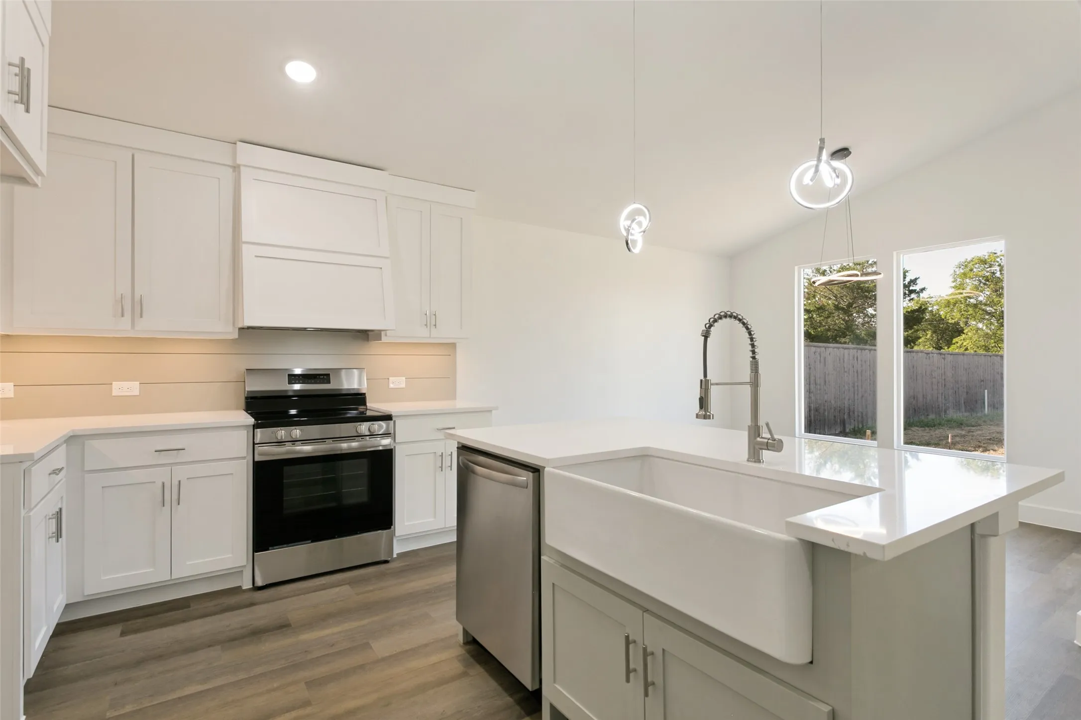 White shaker cabinetry with stainless steel appliances, a farmhouse sink, light countertops, wood-finish flooring, and pendant lighting