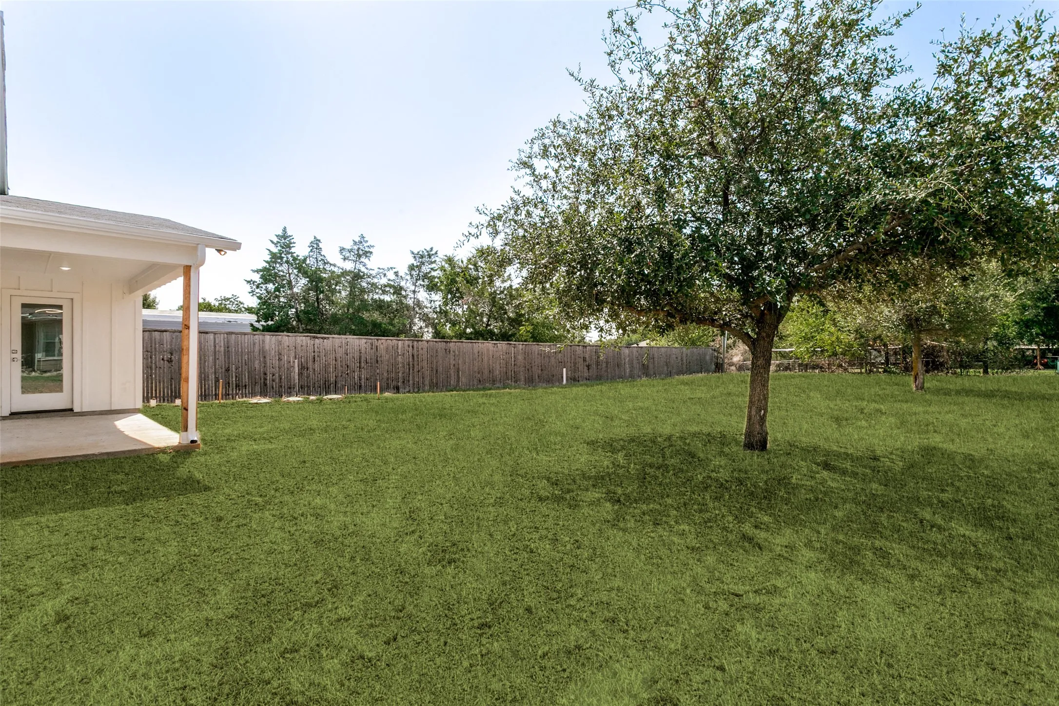 Expansive green lawn featuring mature trees and a wooden privacy fence