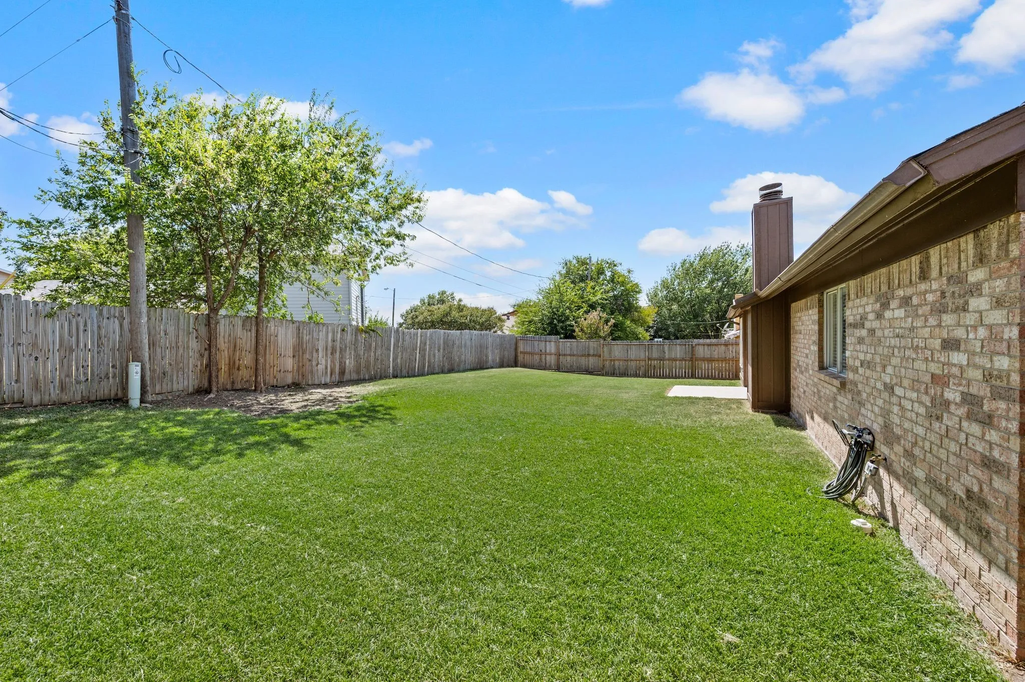 Expansive backyard with mature landscaping, lush manicured lawn, and wooden privacy fencing
