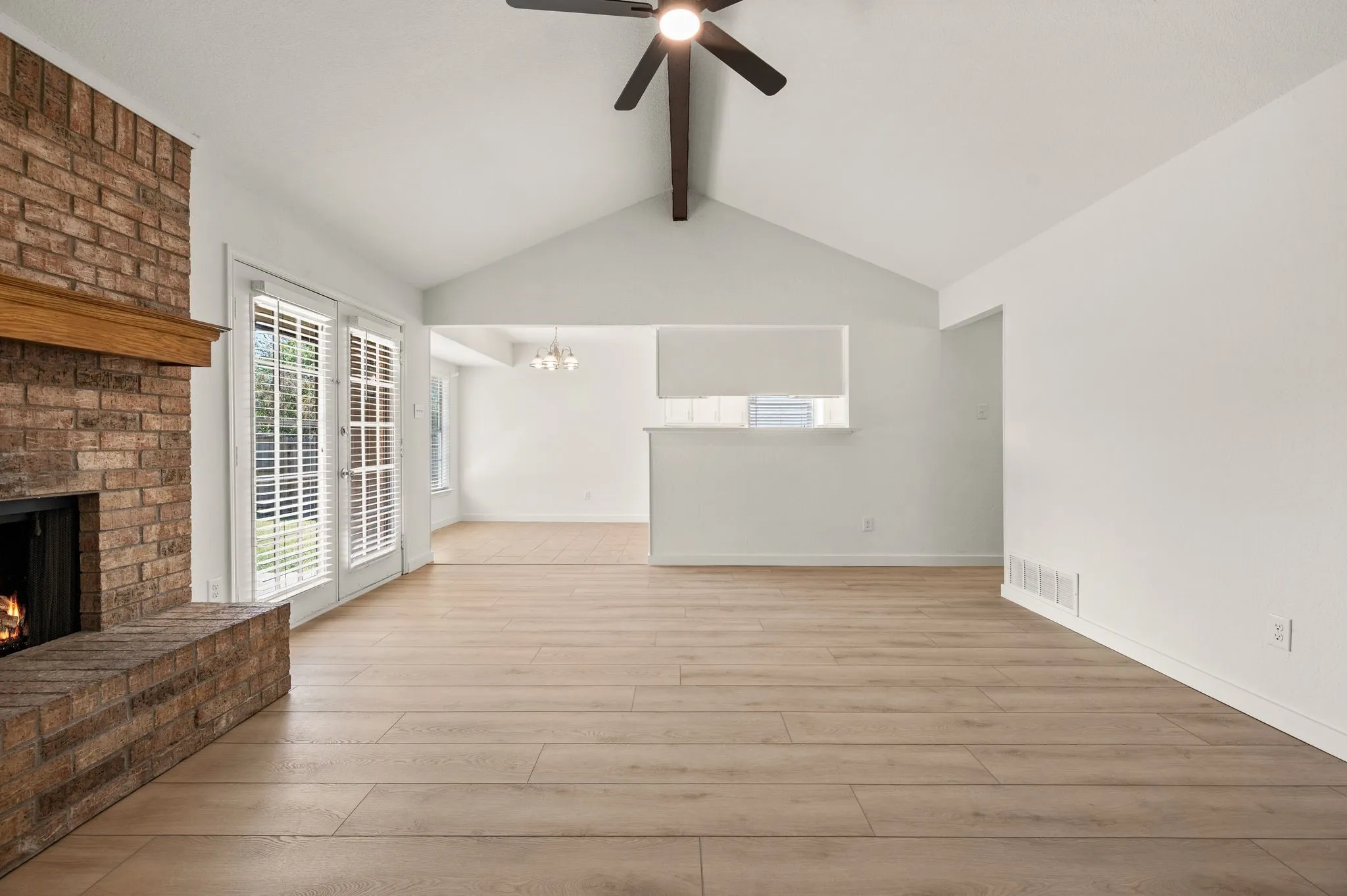 Spacious open-concept living area featuring wood-finish flooring, vaulted ceiling with ceiling fan, and abundant natural light from multiple windows