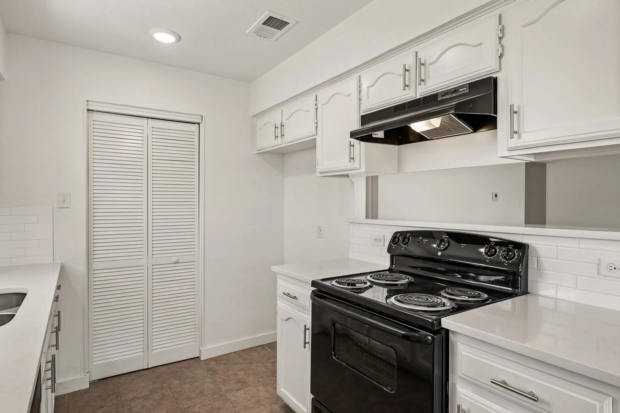 Galley kitchen featuring white cabinetry with chrome hardware, black gas range with multiple burners and convection oven, stainless steel range hood, subway tile backsplash, and wood-finish flooring