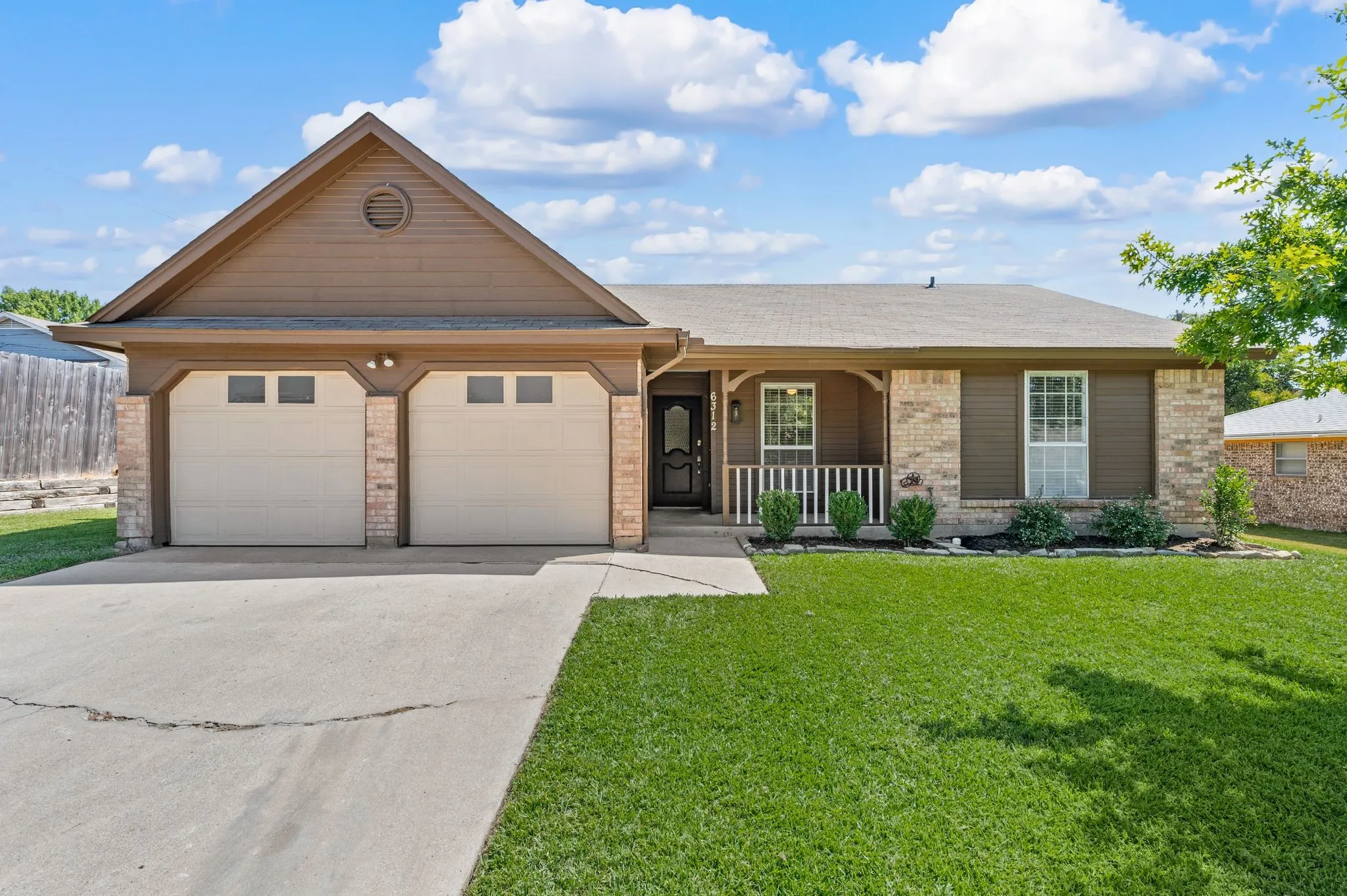 Welcoming brick and stone exterior with a covered front porch, dual two-car garage, and manicured lawn