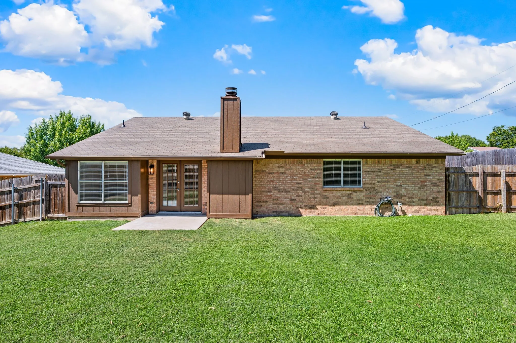 Charming brick ranch with a modern wood-finish entry, large picture windows, and a chimney accent