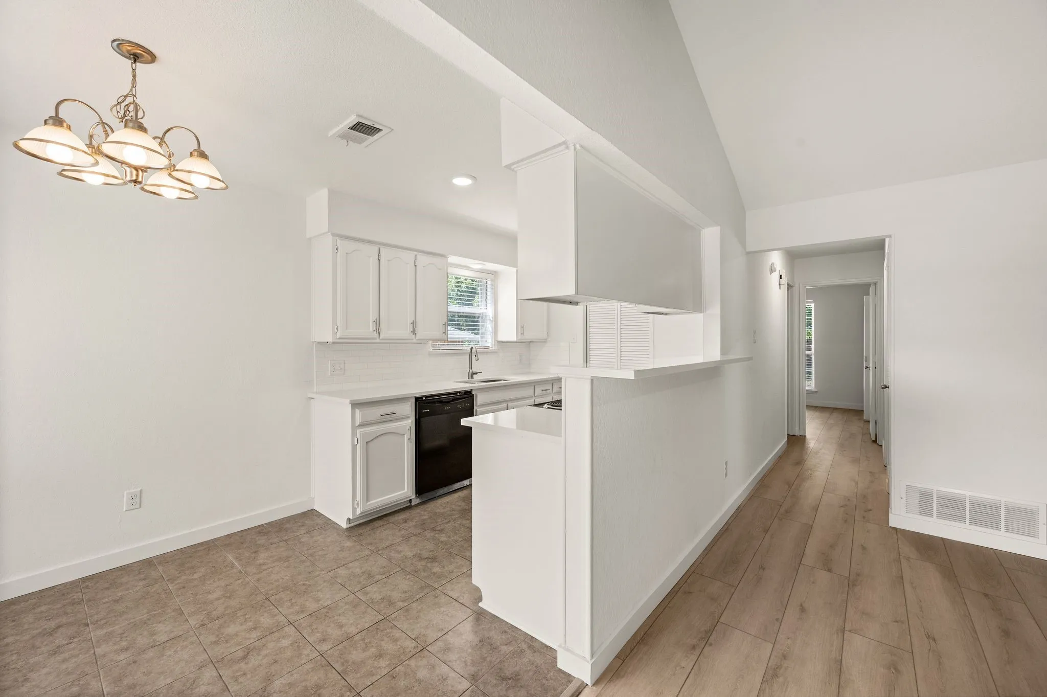 Vaulted ceiling, wood-finish flooring, tiled flooring, white cabinetry, and a kitchen pass-through