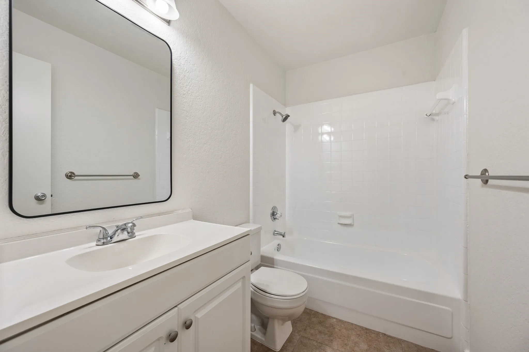 Clean and functional bathroom featuring a white vanity with integrated sink, framed mirror with black trim, white subway tile shower surround with glass enclosure, and chrome fixtures throughout