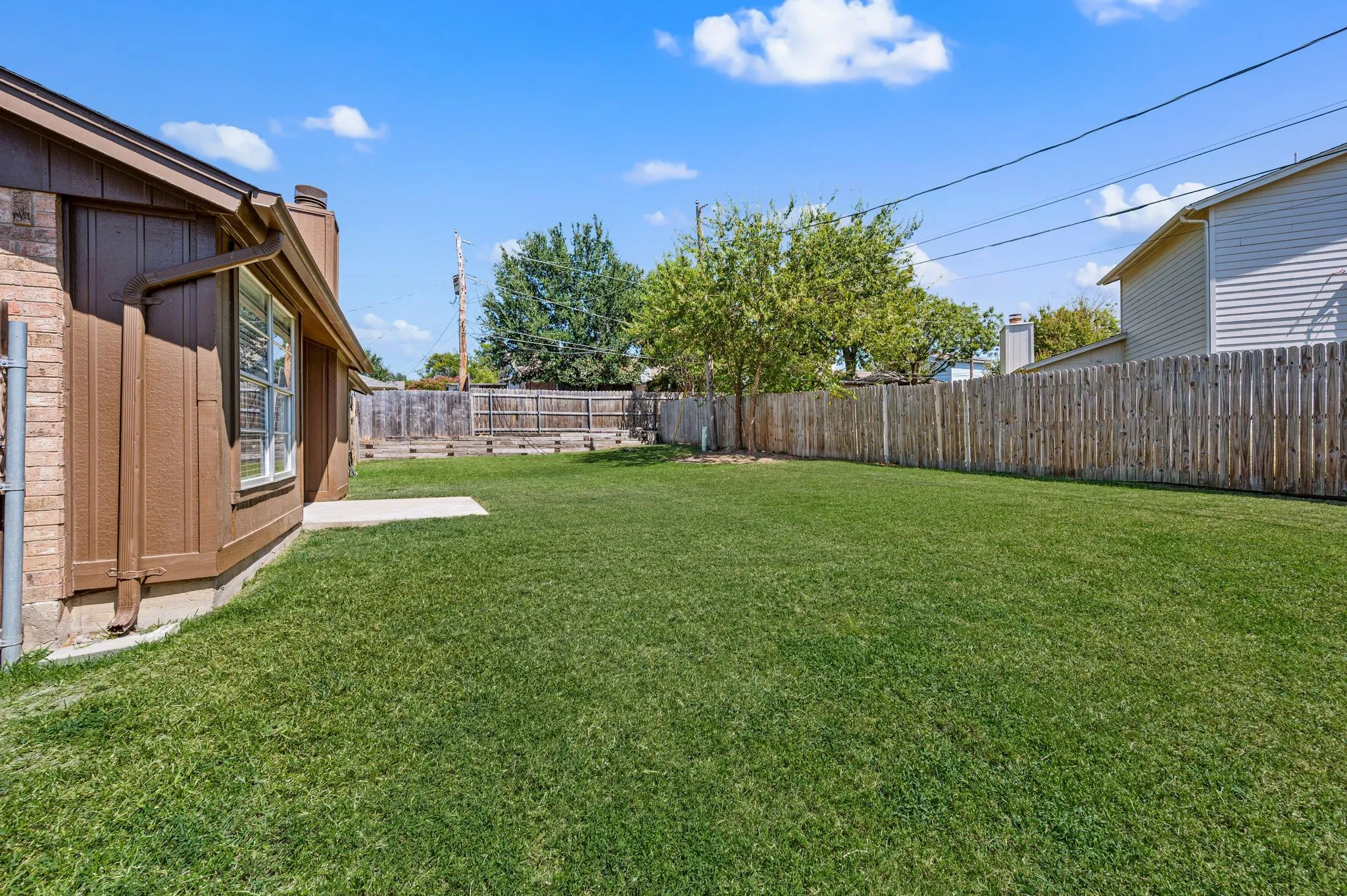 Expansive backyard featuring a manicured lawn, mature shade trees, and wooden privacy fencing