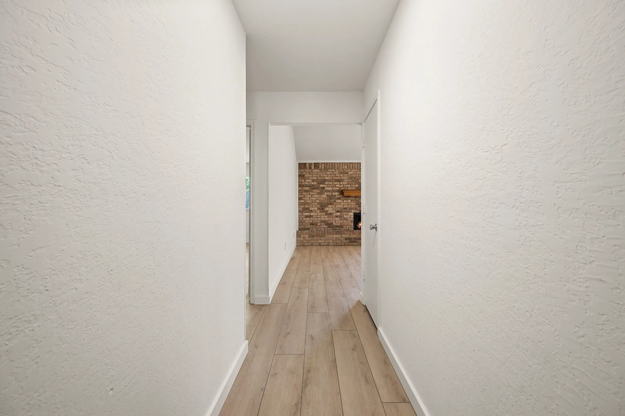 Bright hallway with clean white textured walls, warm wood-finish flooring, and generous ceiling height