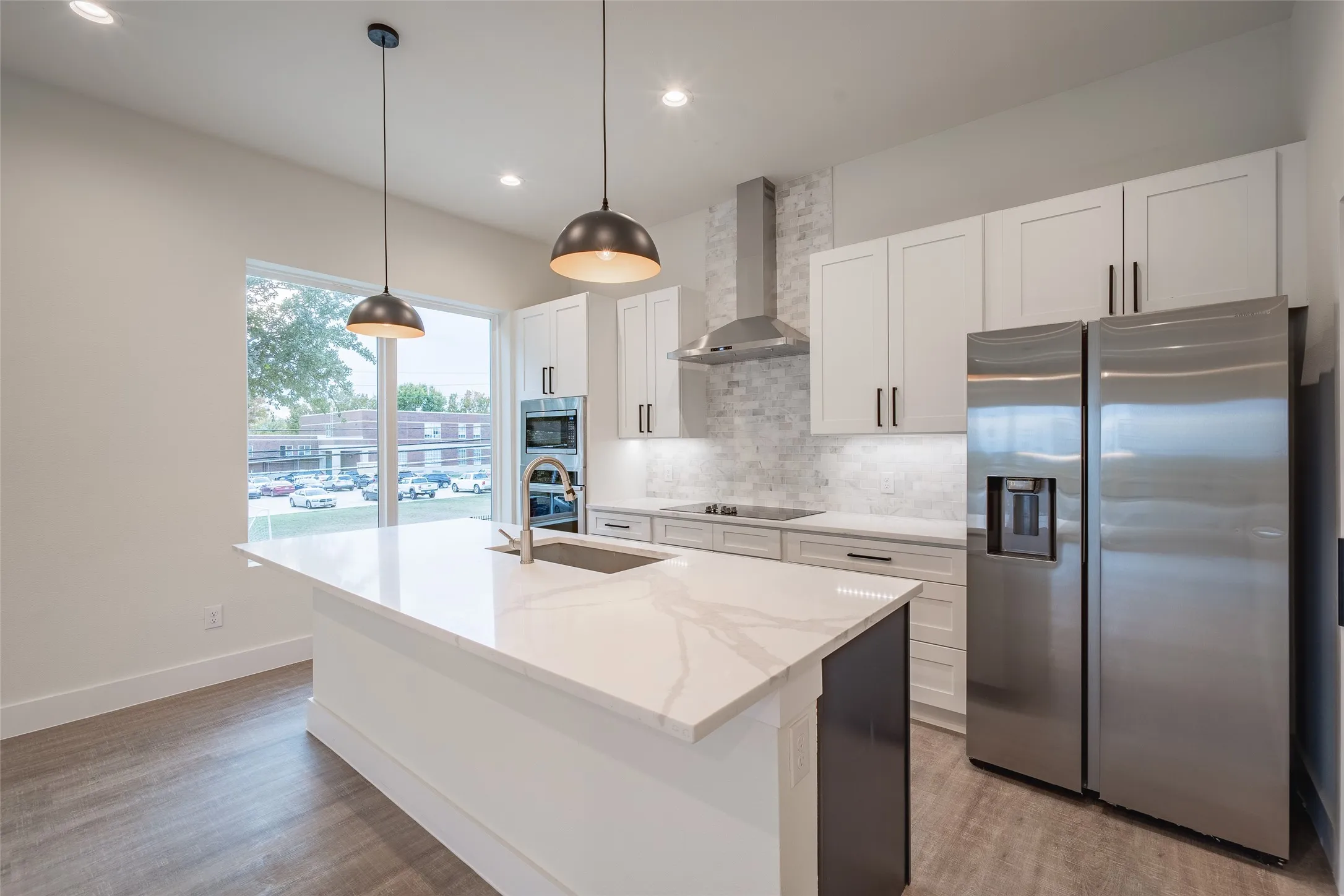 Kitchen featuring white cabinets, an island with sink, wall chimney range hood, and appliances with stainless steel finishes