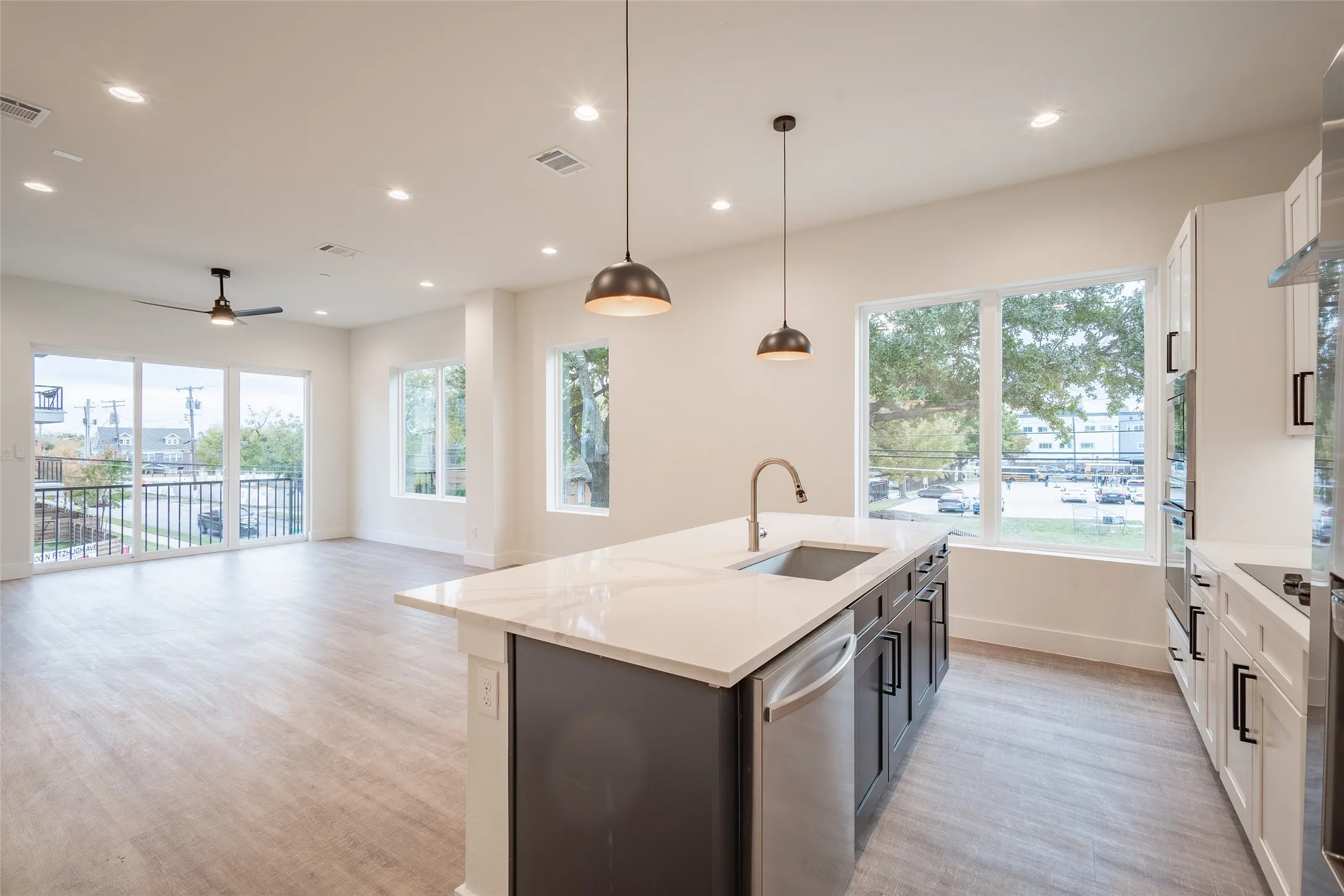 Kitchen featuring a kitchen island with sink, sink, decorative light fixtures, white cabinetry, and stainless steel appliances