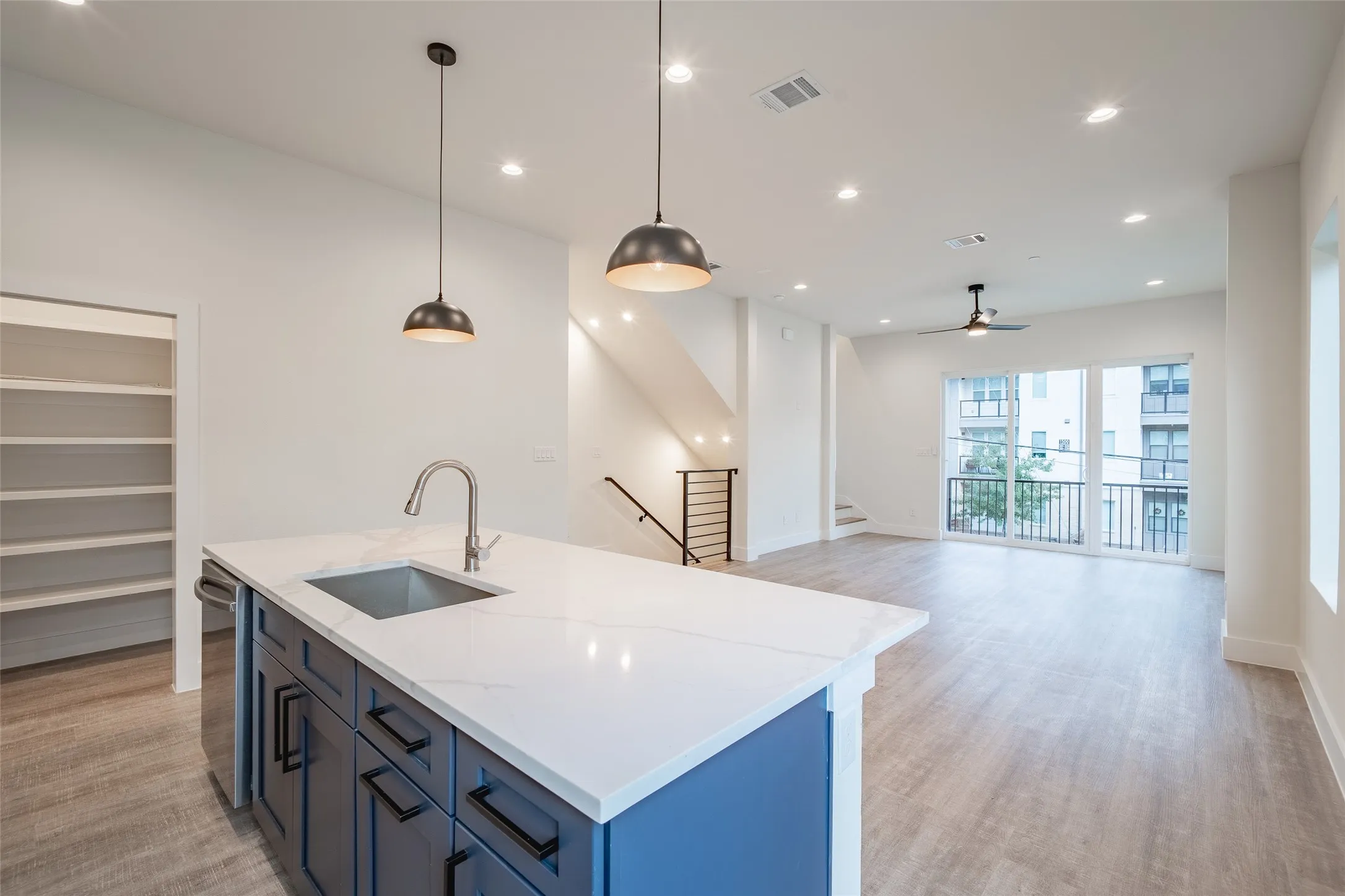 Kitchen featuring ceiling fan, sink, hanging light fixtures, light stone counters, and light hardwood / wood-style floors