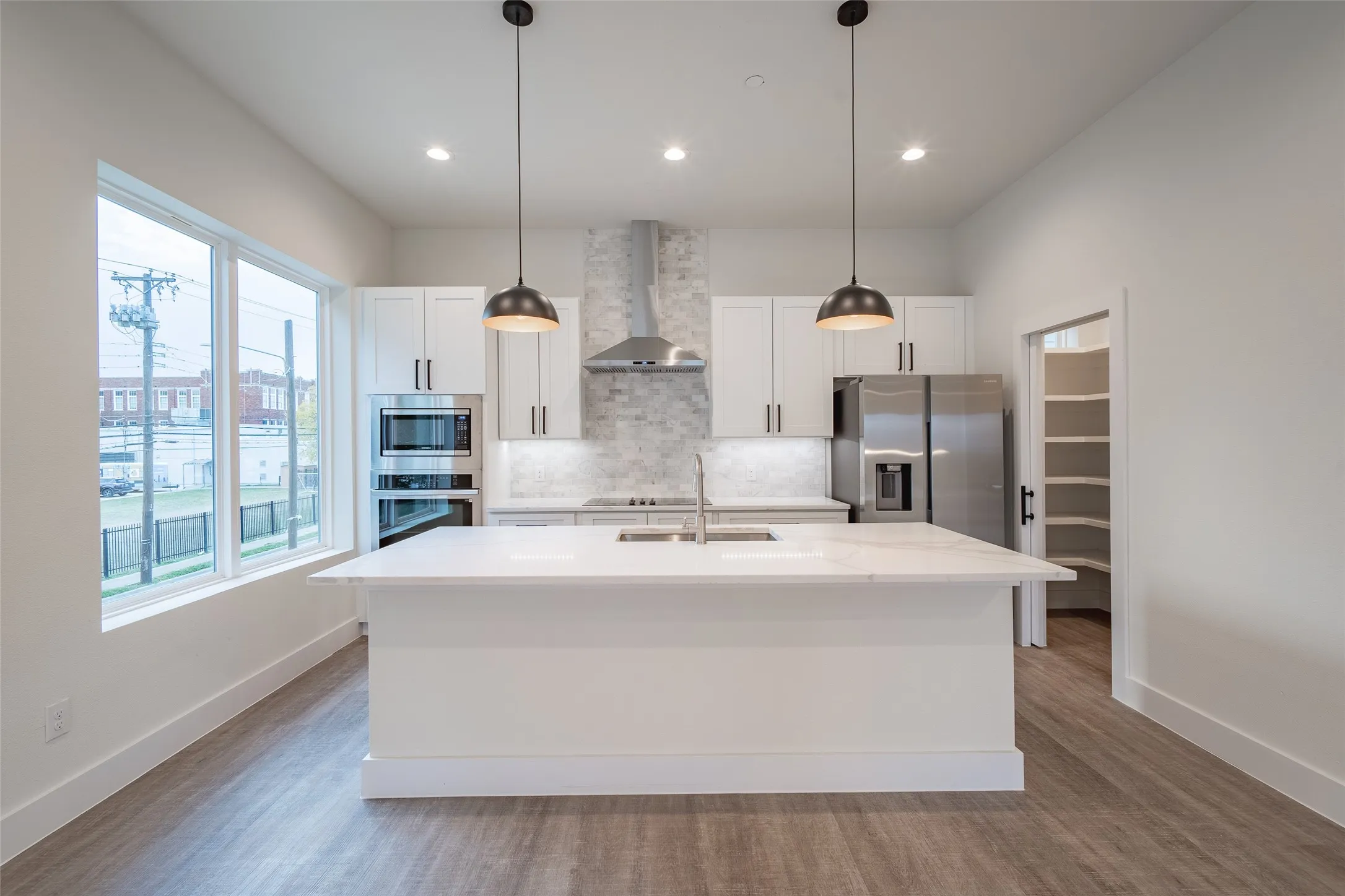 Kitchen featuring stainless steel appliances, sink, wall chimney range hood, white cabinetry, and an island with sink