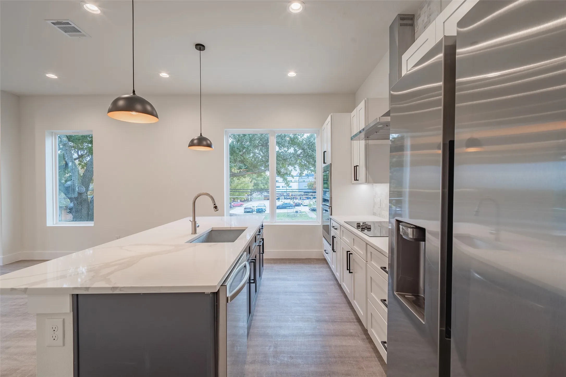 Kitchen featuring a kitchen island with sink, white cabinetry, stainless steel appliances, and decorative light fixtures