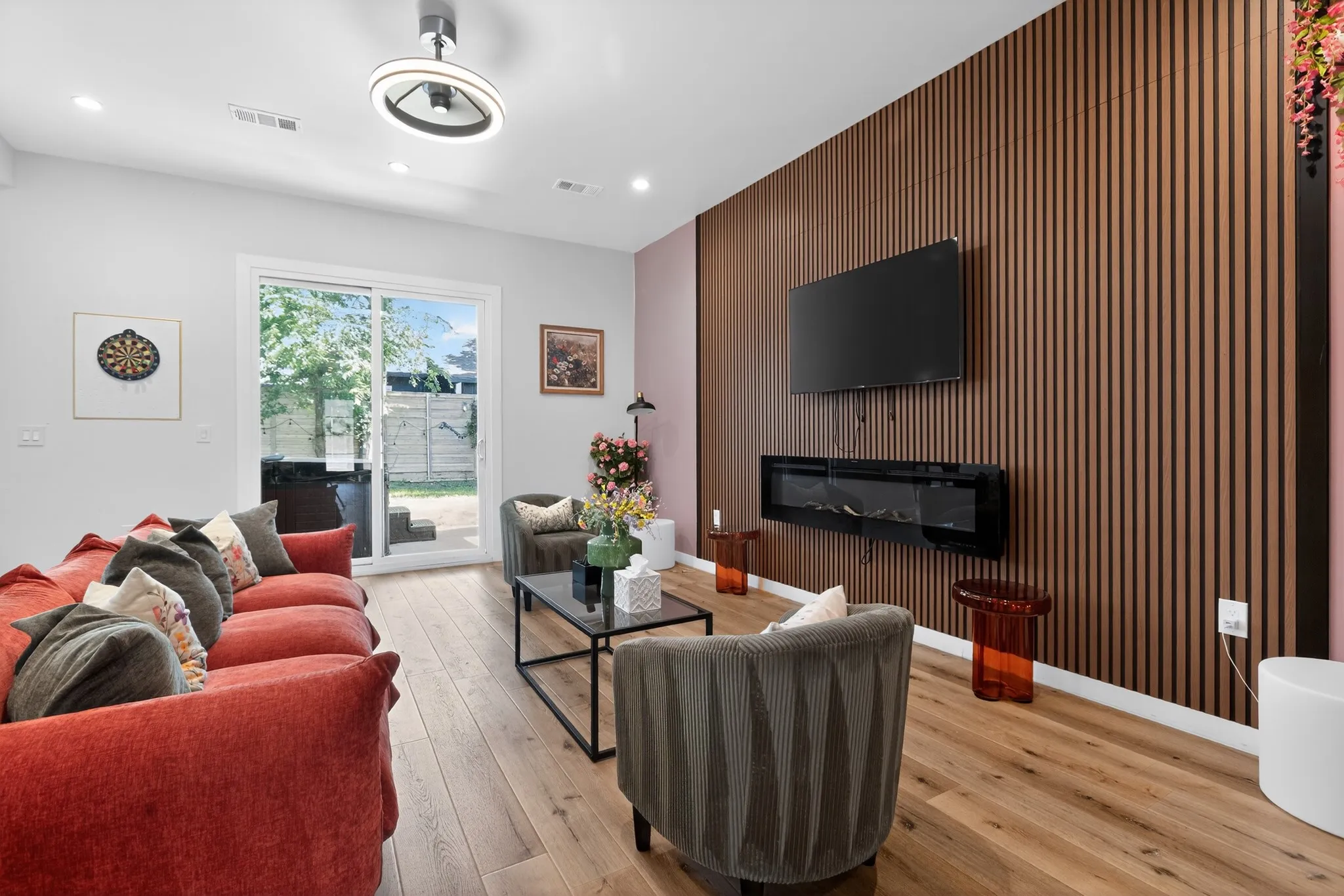 Wood-finish flooring, accent wall with vertical wood paneling, wall-mounted electric fireplace, sliding glass door, and recessed lighting