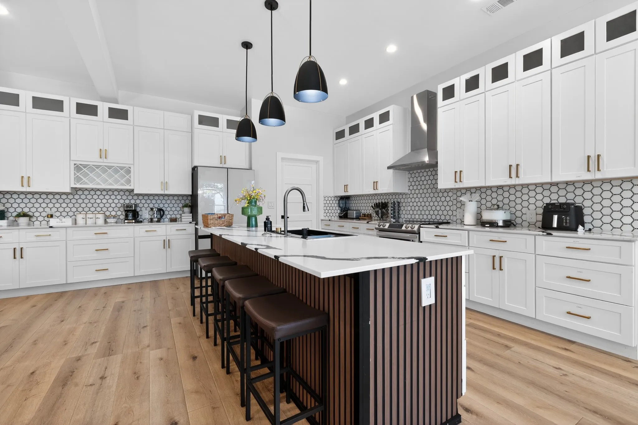 Expansive kitchen with a large central island, white cabinetry, hexagon tile backsplash, and wood-finish flooring