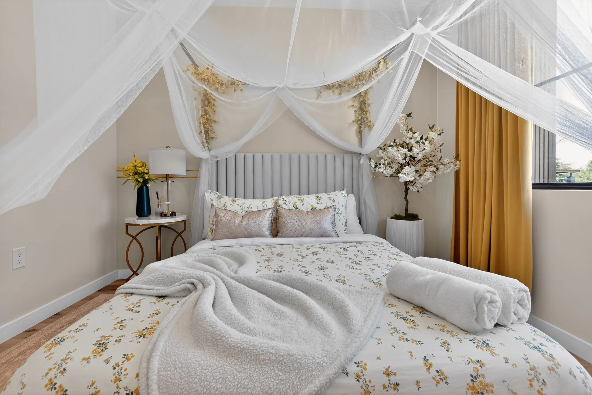 Light wood-finish flooring, light grey channel-tufted headboard, and a window with a dark frame