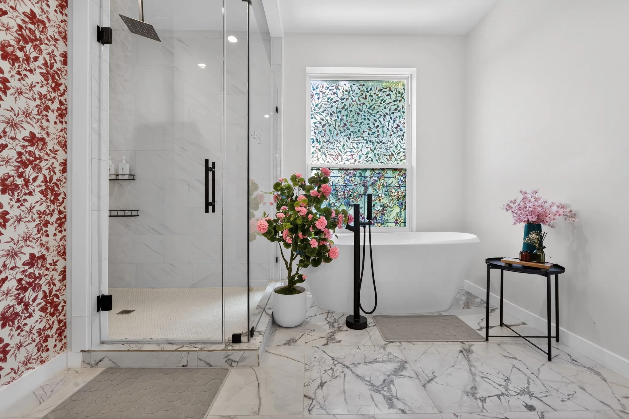 Freestanding soaking tub with a floor-mounted matte black faucet, glass-enclosed shower with a rainfall showerhead, and white marble-look tile flooring