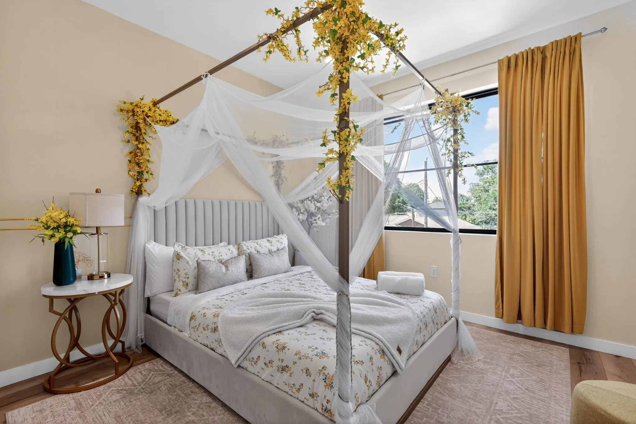Recessed paneled headboard, wood-finish flooring, large window with expansive window treatment, and neutral wall color
