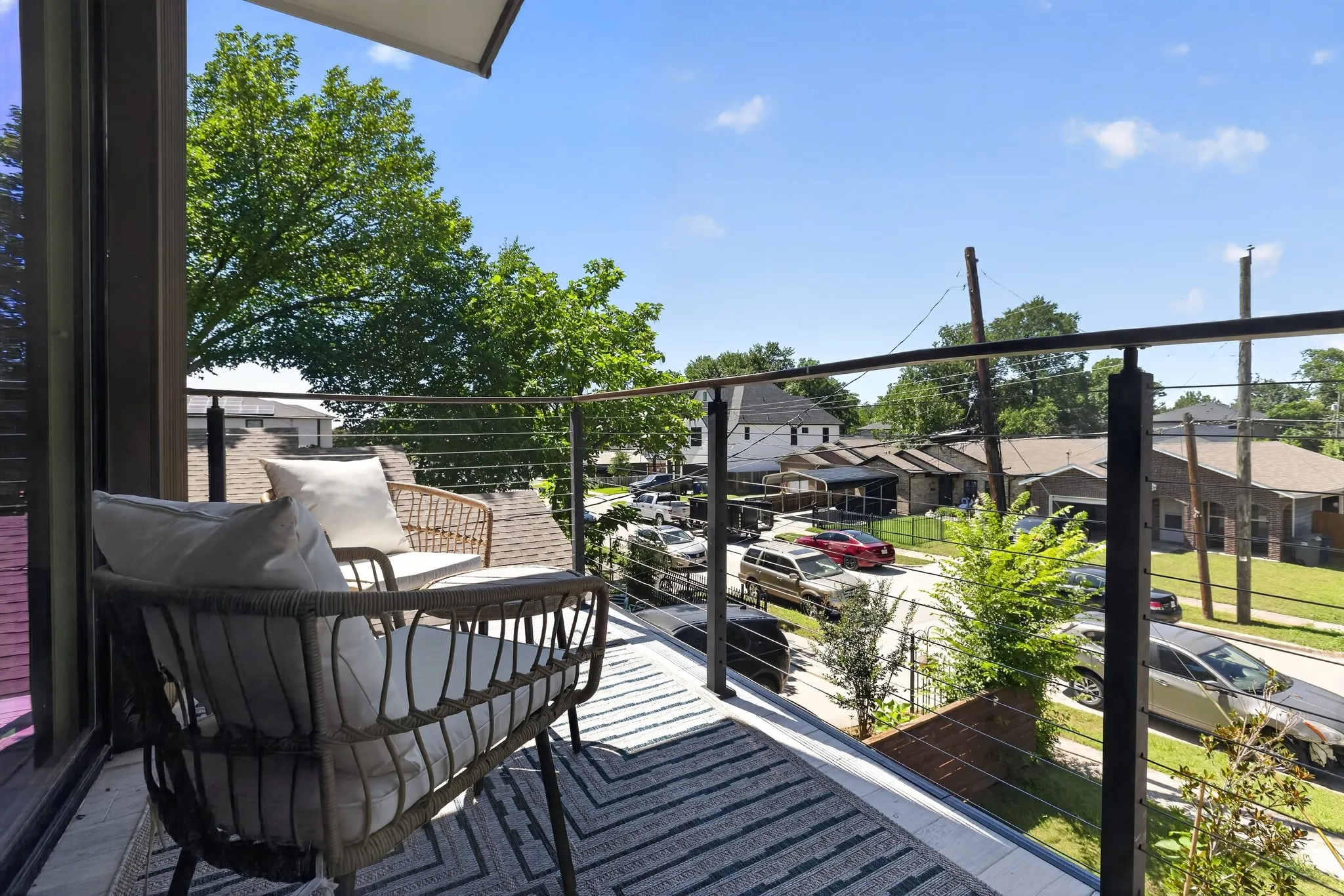 Private balcony featuring a cable railing system, dark window framing, and a partial awning
