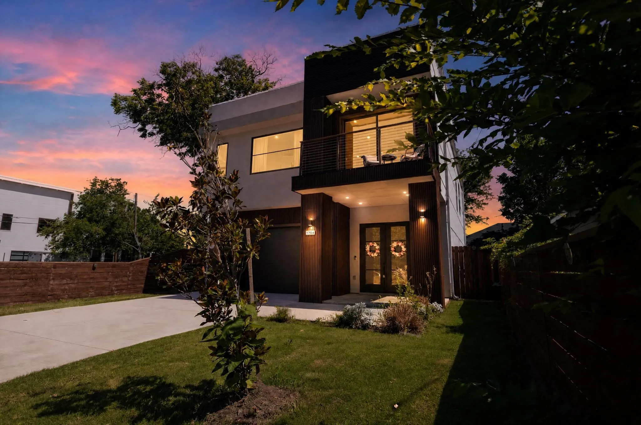 Contemporary exterior with a balcony, an attached garage, a concrete driveway, and a fenced yard