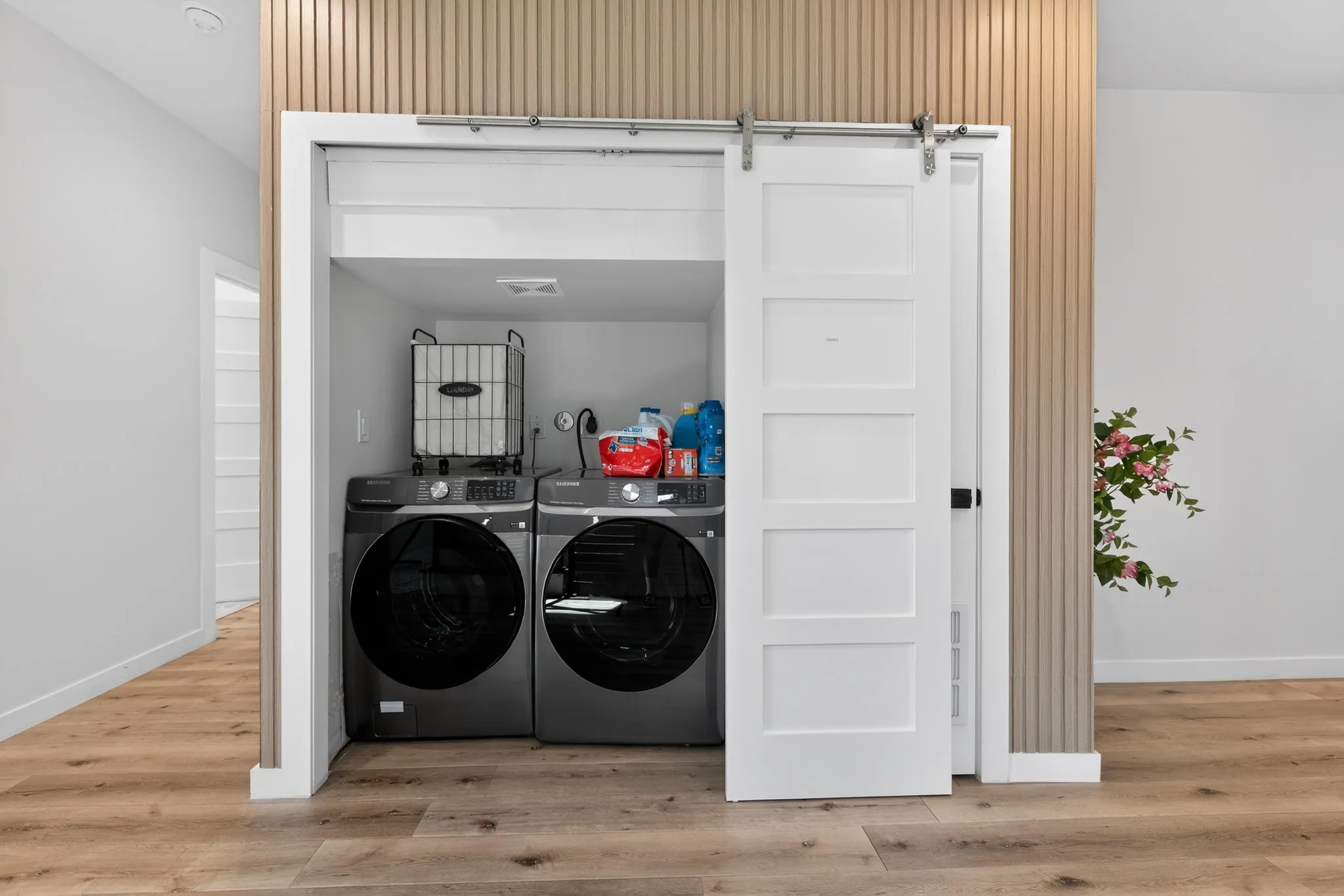 Laundry closet with white barn door, wood-finish flooring, and slatted accent wall