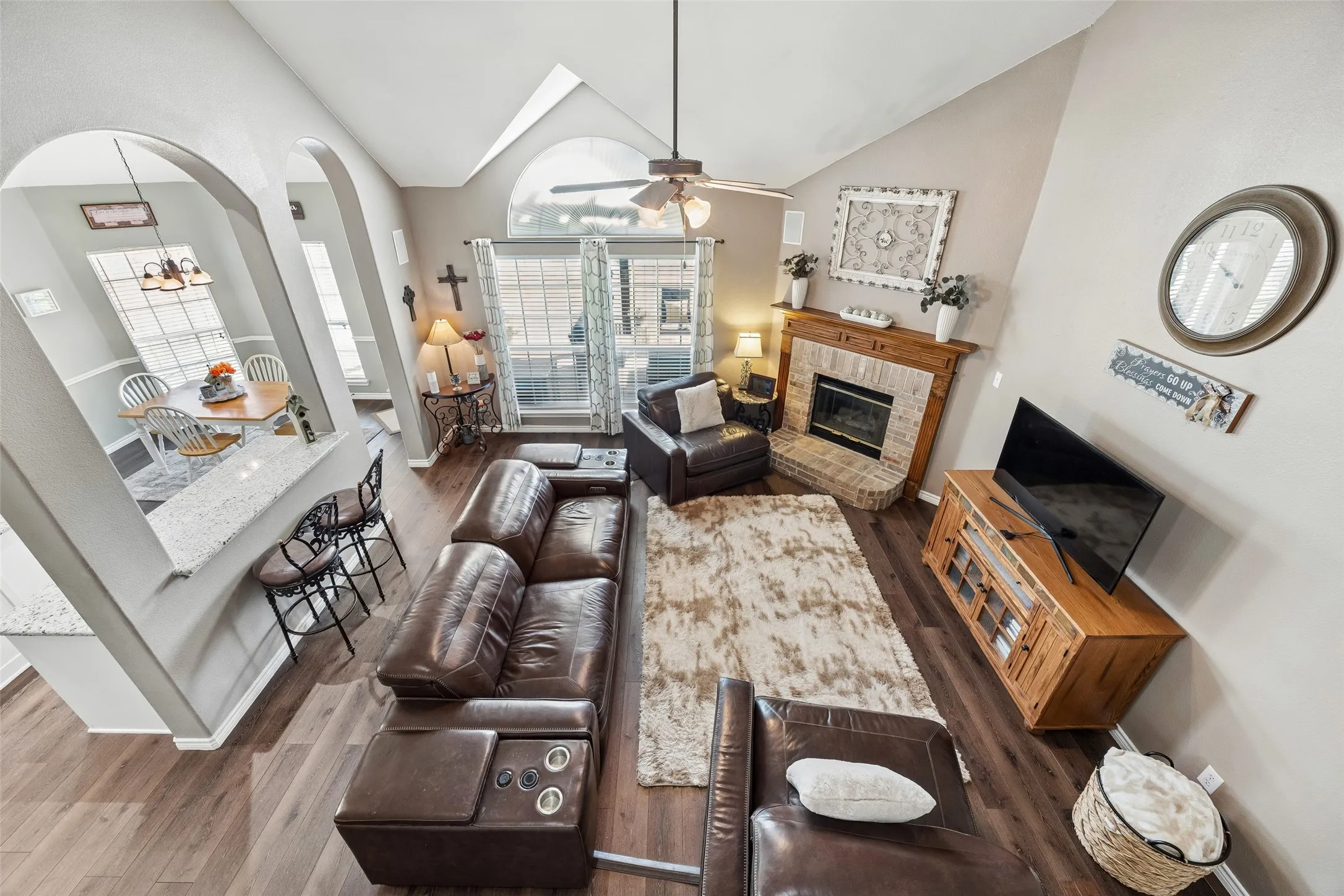 View from Above Shows the Open Floor Plan — From the upstairs overlook, you can see how the family room, kitchen pass-through, and breakfast area relate to one another. The vaulted family room, arched openings, large windows, and fireplace give the main living space plenty of architectural character.